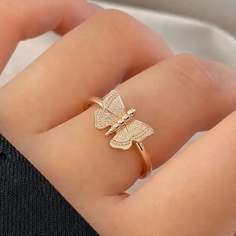 Rose gold butterfly ring on a person's finger with a neutral background
