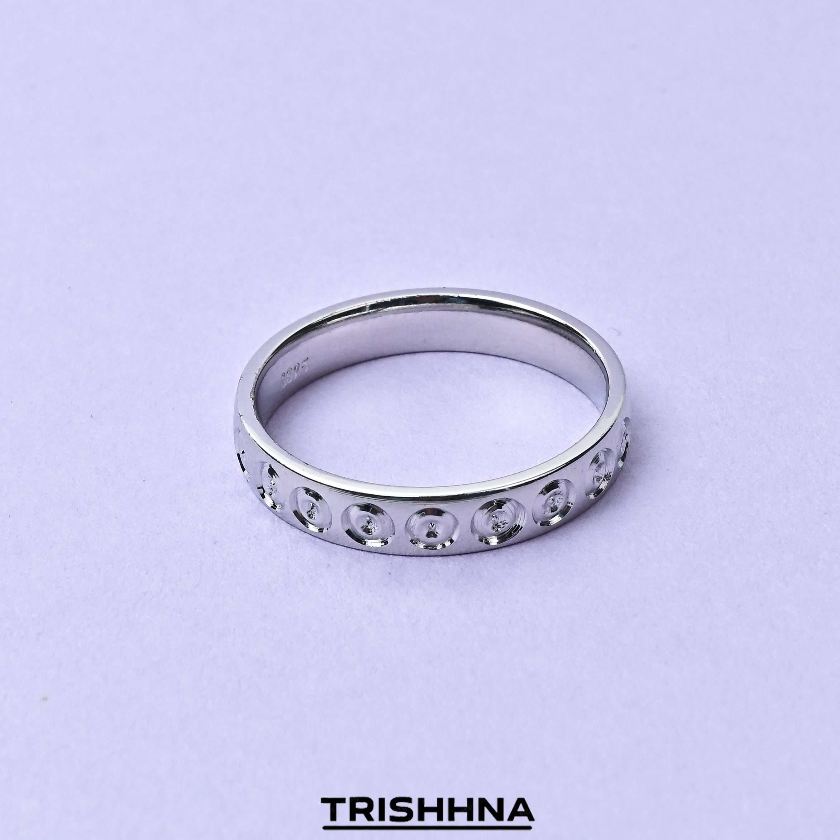 Silver ring with small stones on a light purple background, branded 'TRISHNHA'.