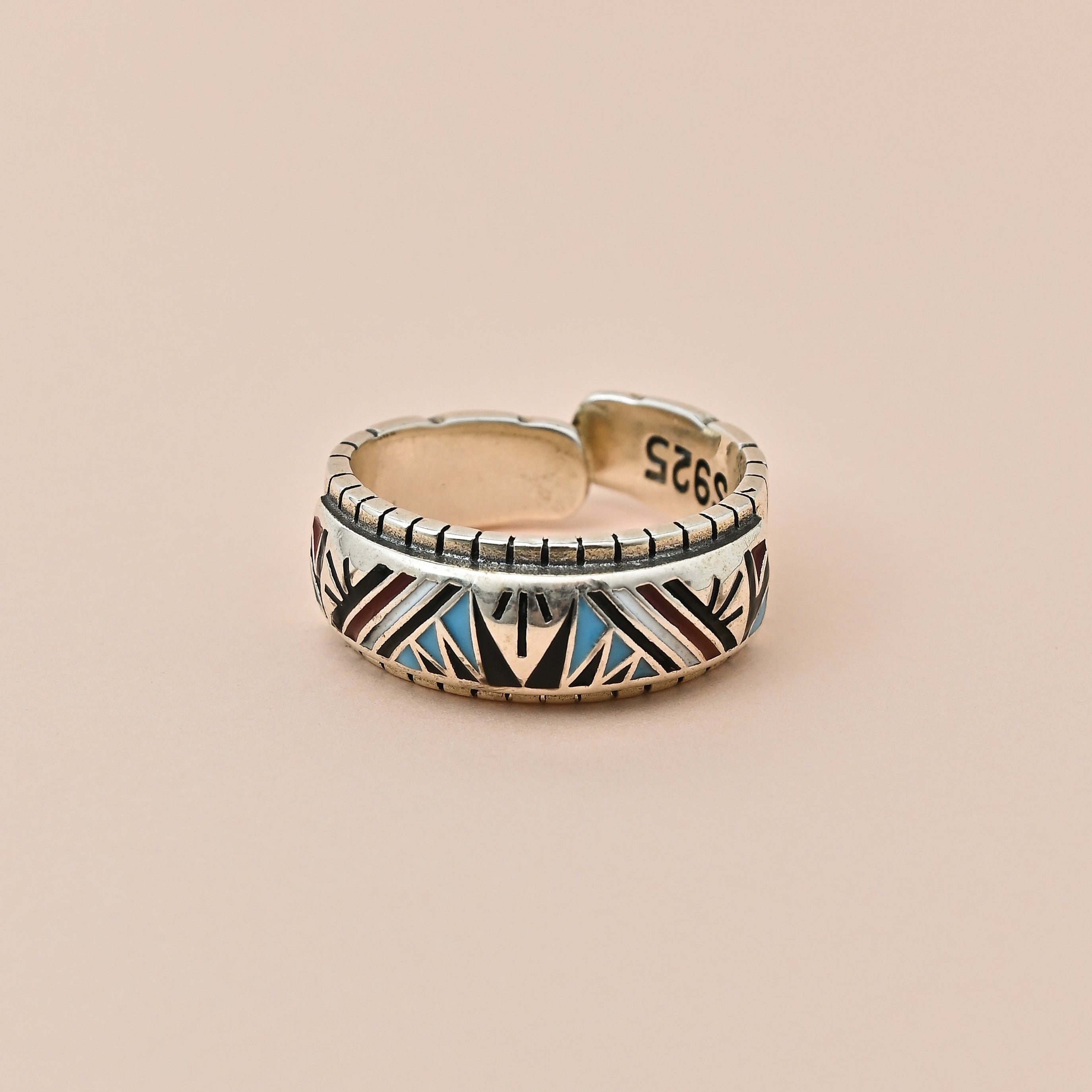 Gold and silver ring with blue accents on a beige background, featuring the brand 'Trishna'.