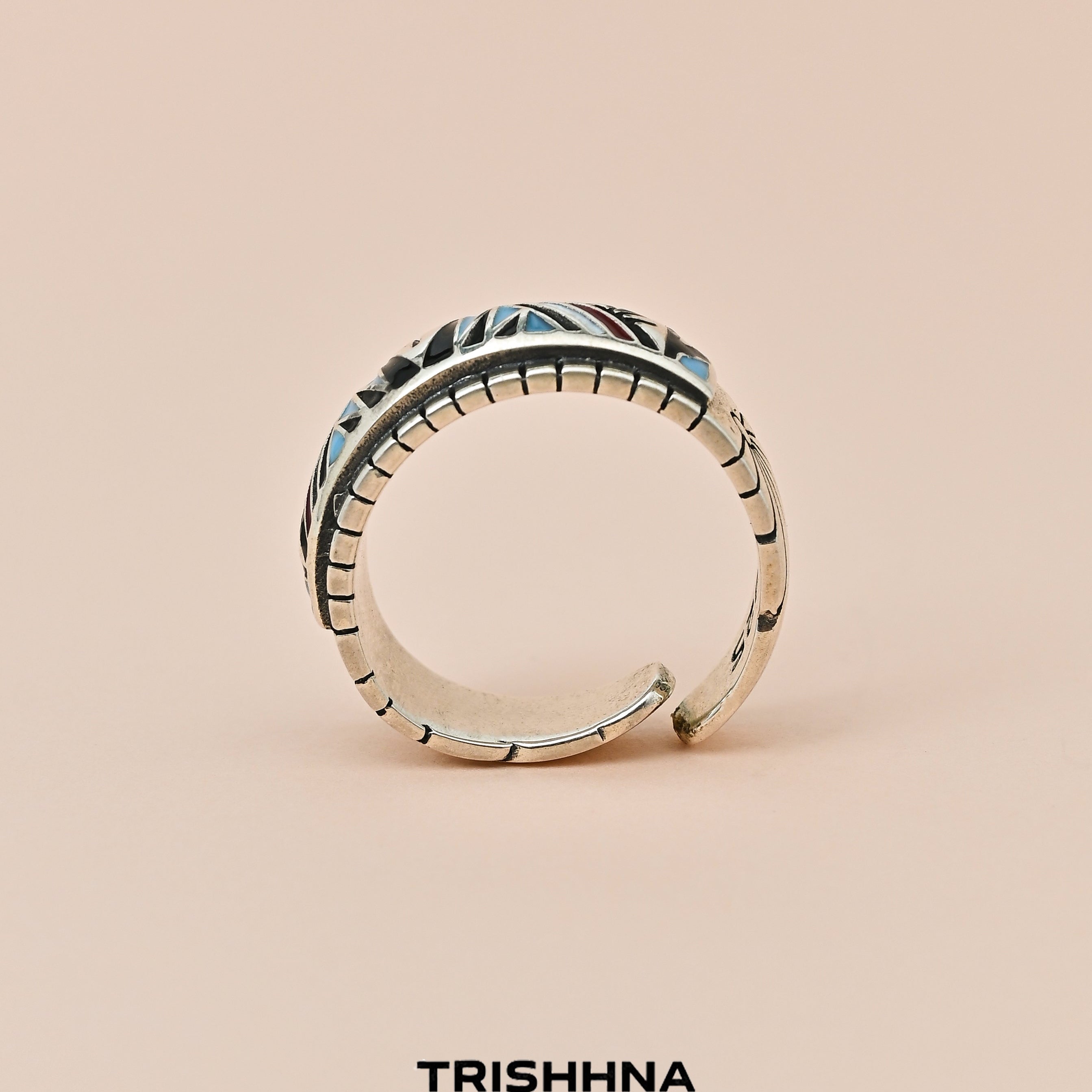 Silver ring with intricate design on a beige background, featuring the brand 'TRISHNHA'.