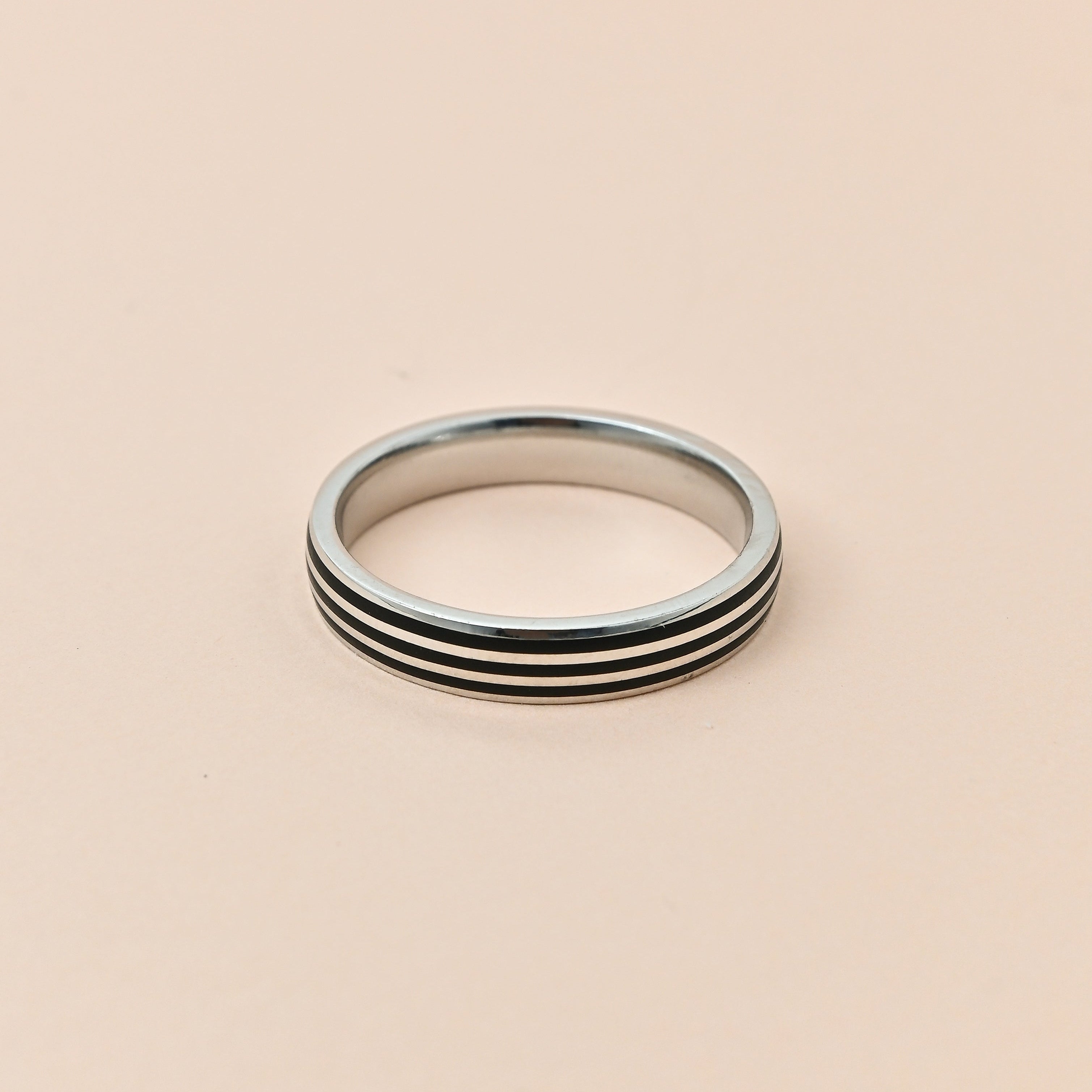 Silver ring with black stripes on a beige background, featuring the brand 'TRISHNHA'.