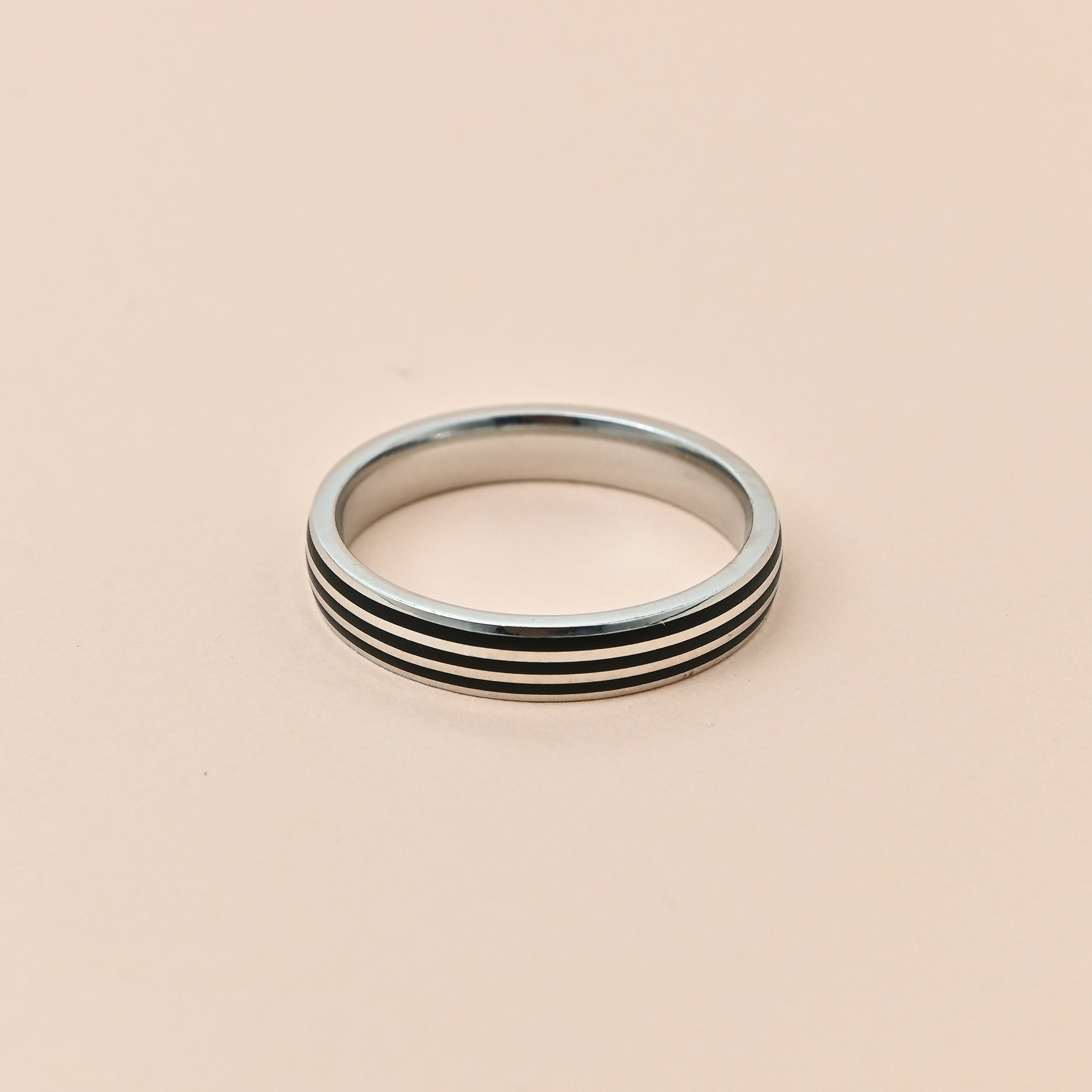 Silver ring with black stripes on a beige background, featuring the brand 'TRISHNHA'.