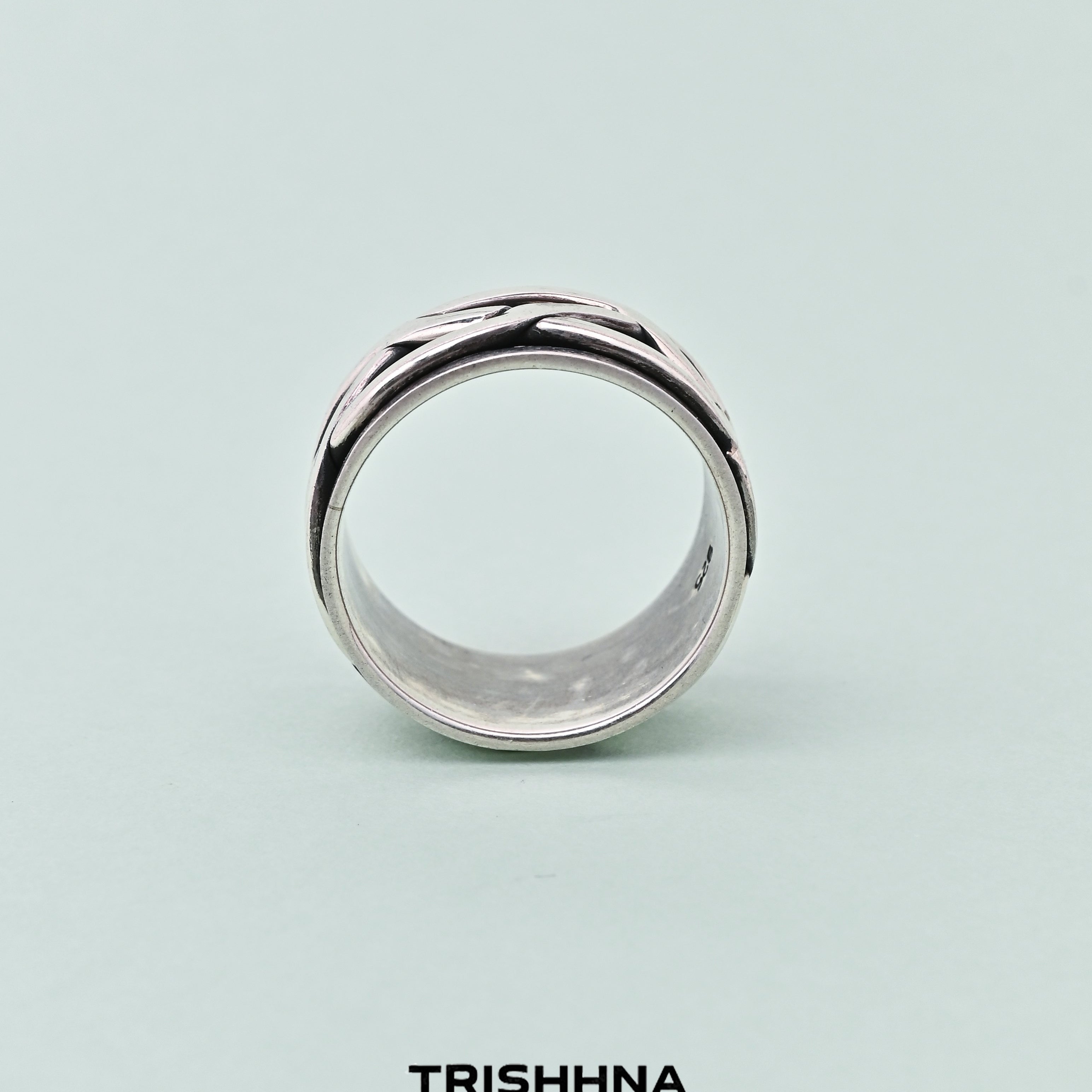 Silver ring with a textured band on a light green background, featuring the brand 'TRISHNHA'.