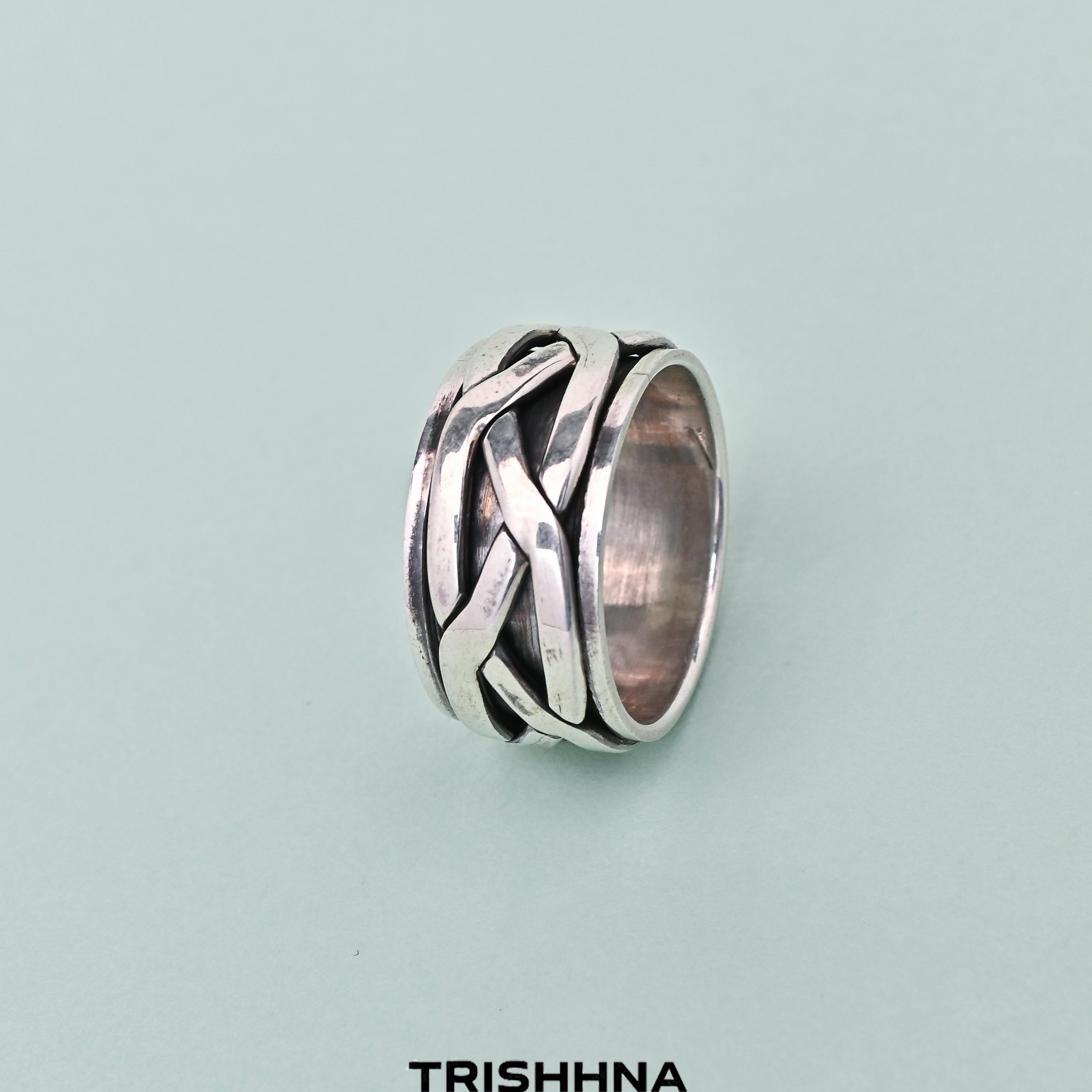 Silver ring with intricate design on a light blue background, branded 'TRISHNHA'.