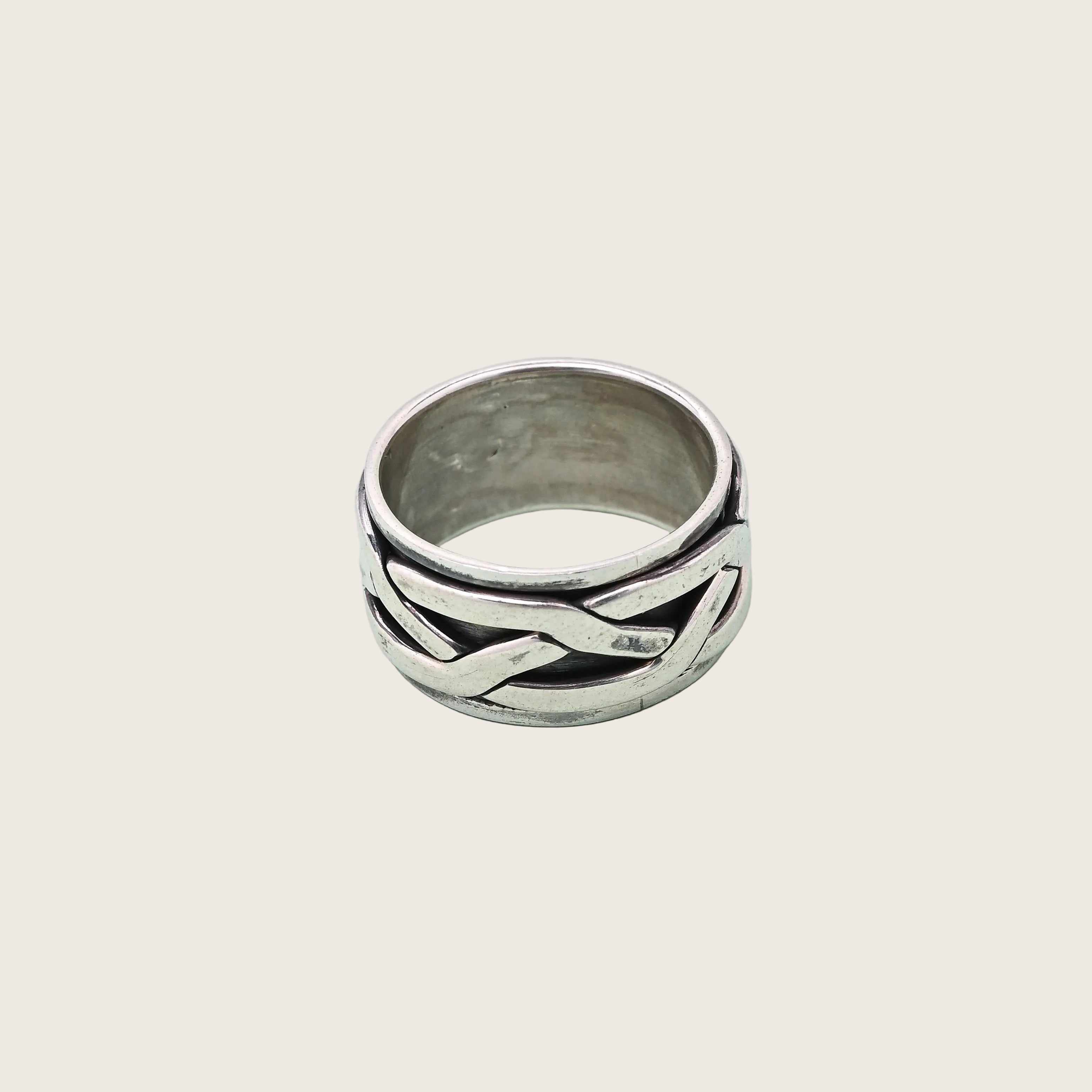 Silver ring with braided design on a light blue background, branded 'TRISHNHA'.