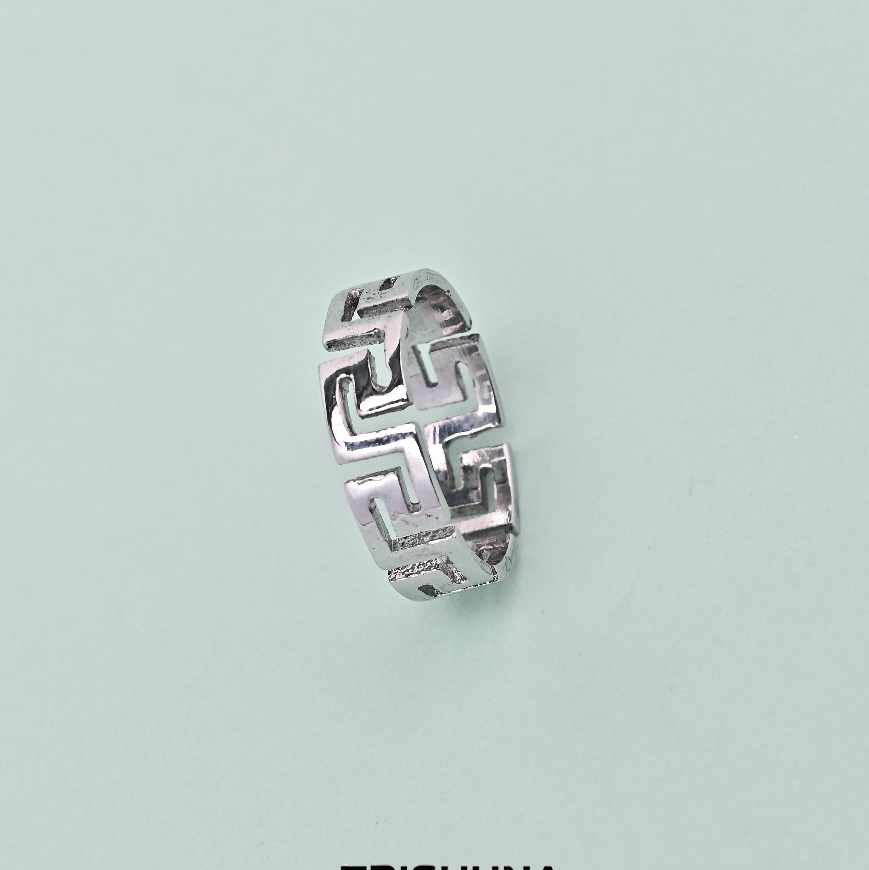 Silver ring with geometric design on a light blue background, featuring the brand 'TRISHNHA'.