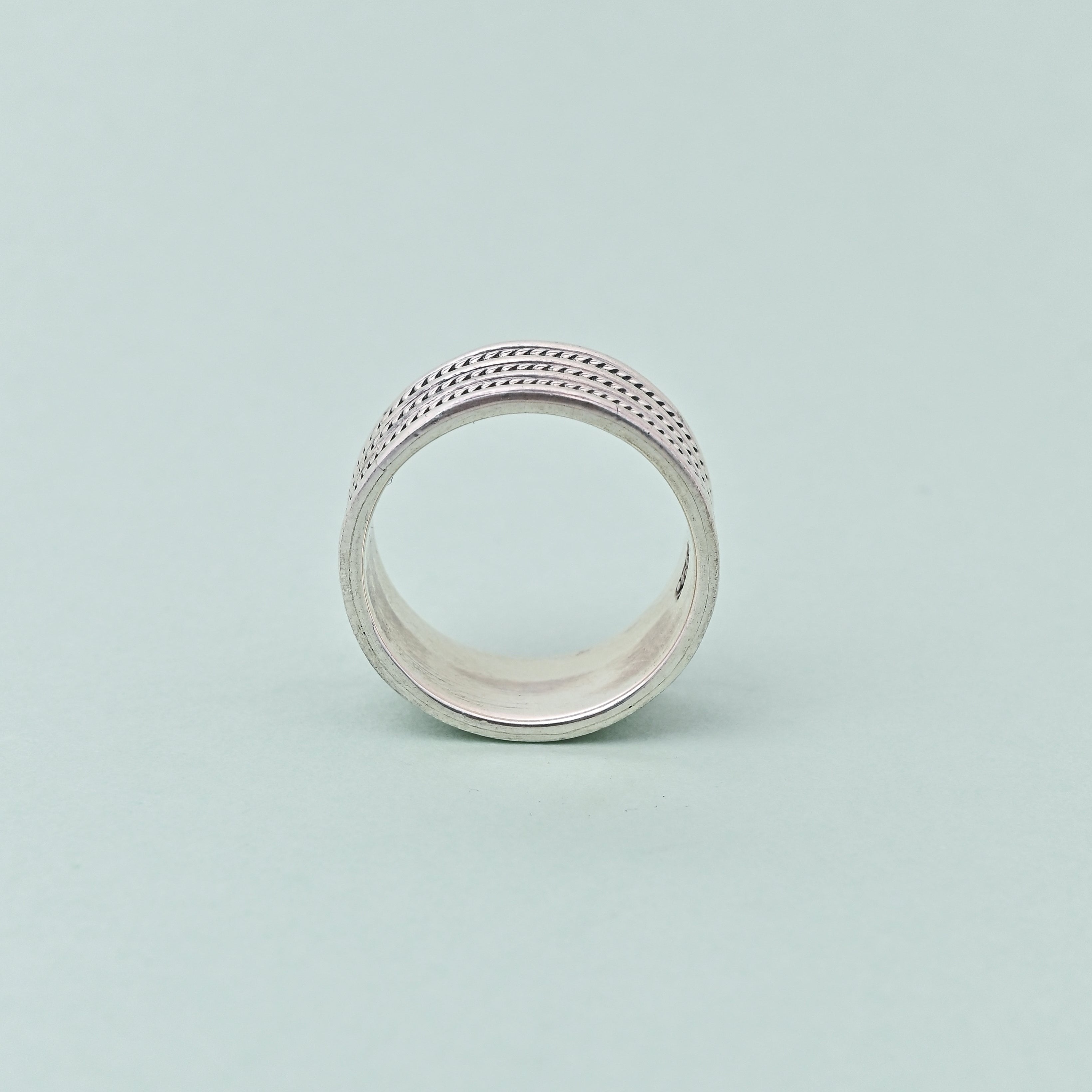 Silver ring with intricate design on a light green background, featuring the brand 'TRISHNNA'.
