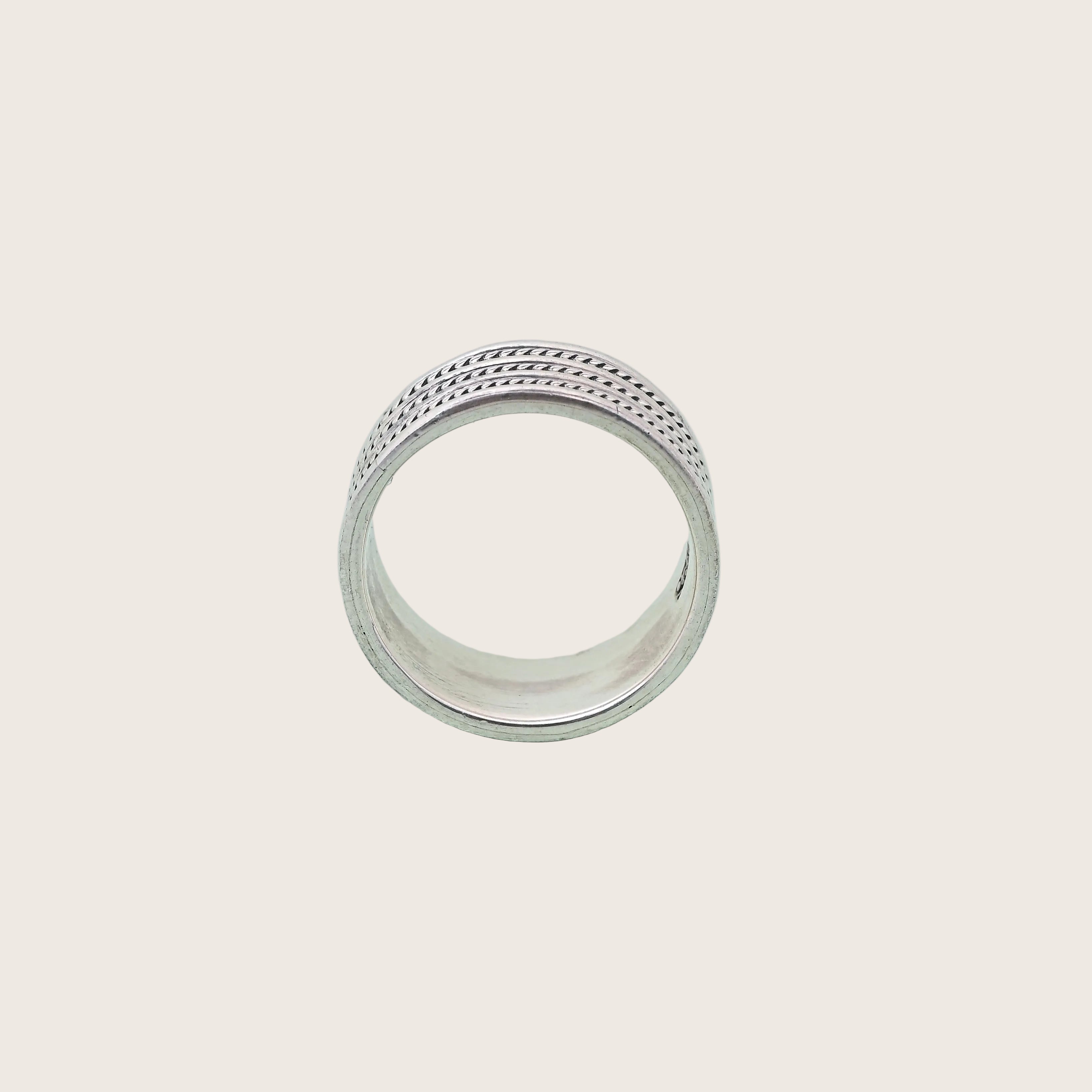 Silver ring with intricate design on a light green background, featuring the brand 'TRISHNNA'.