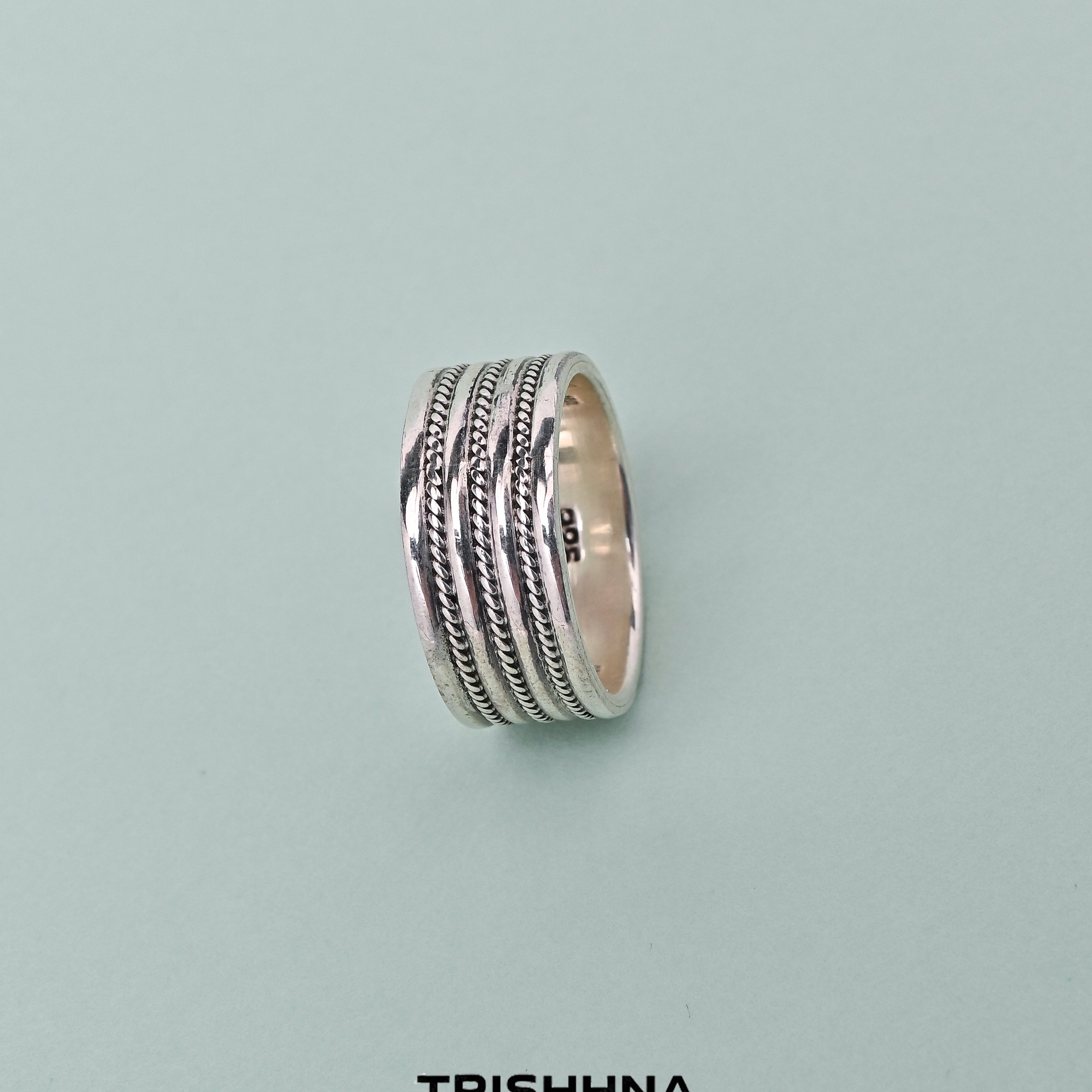 Silver ring with intricate design on a light gray background, featuring the brand 'TRISHNHA'.