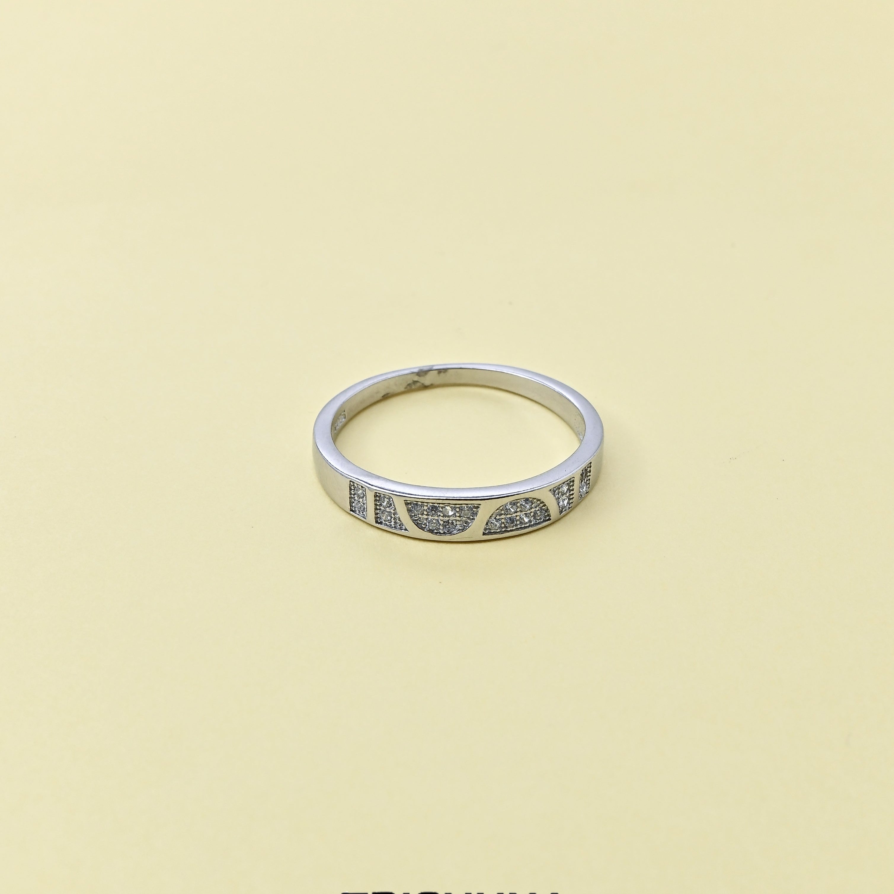 Silver ring with gemstones on a beige background, branded 'TRISHNNA'.