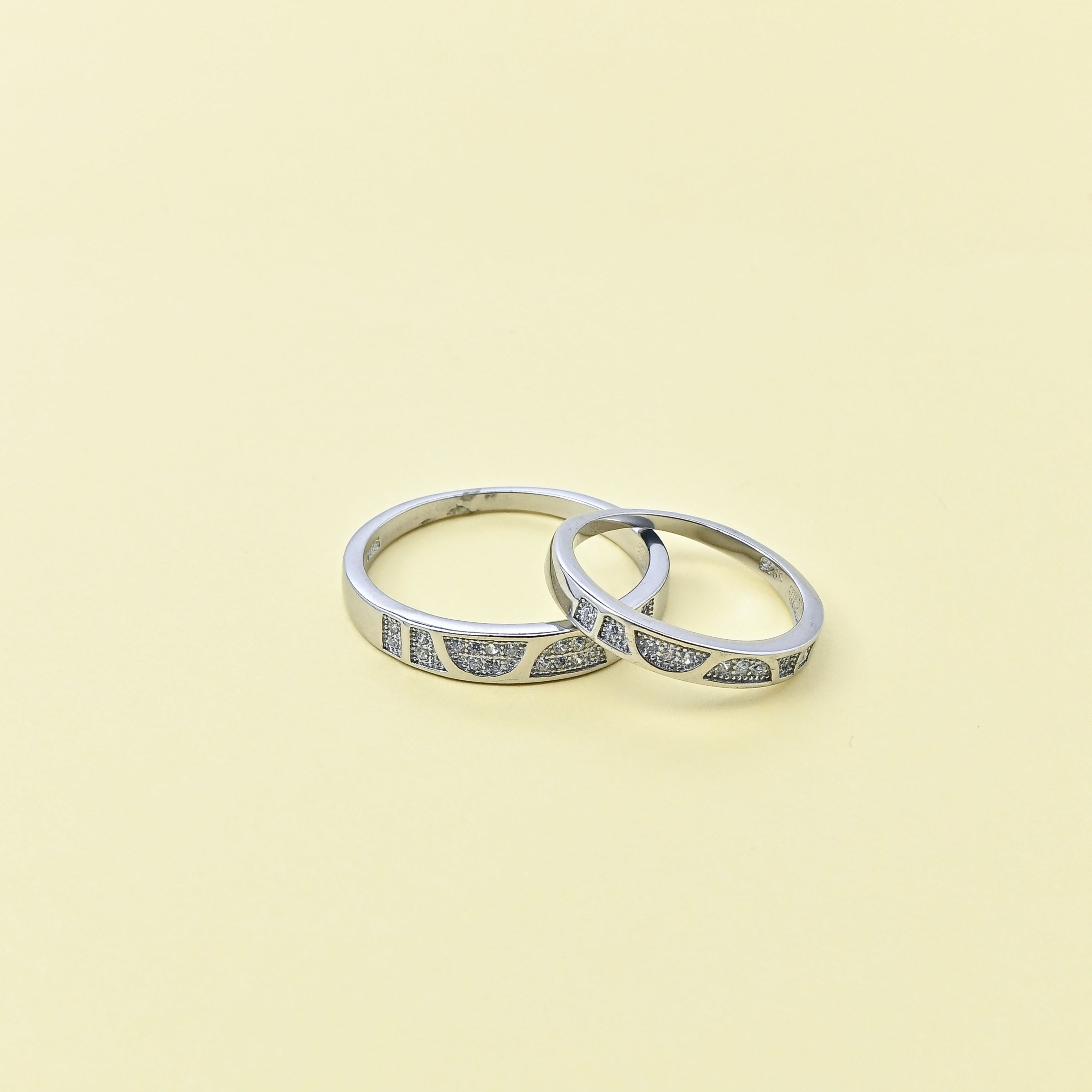Two silver rings with small stones on a beige background, featuring the brand 'TRISHNNA'.
