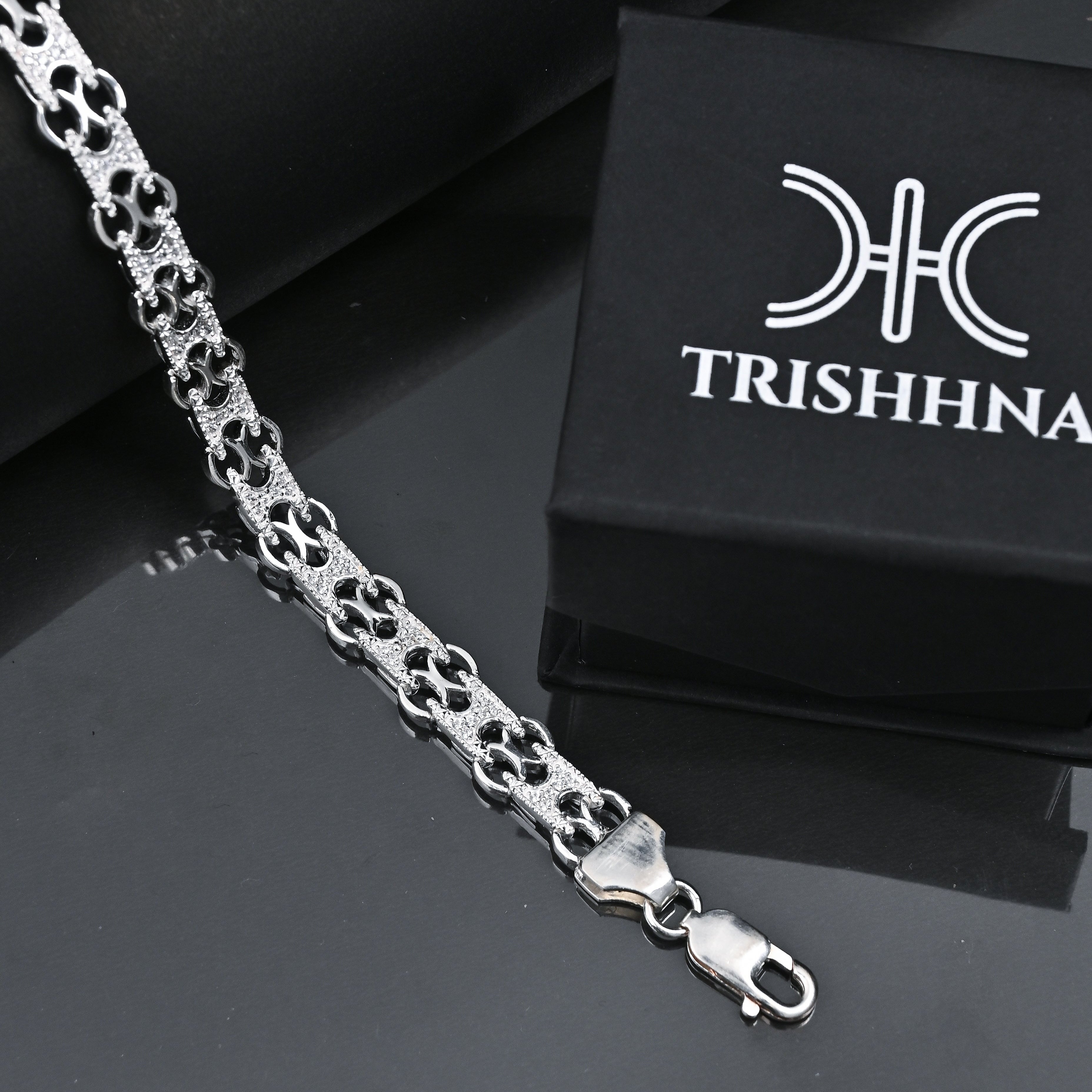 Silver chain bracelet with a black box featuring 'TRISHHNA' branding on a reflective surface.