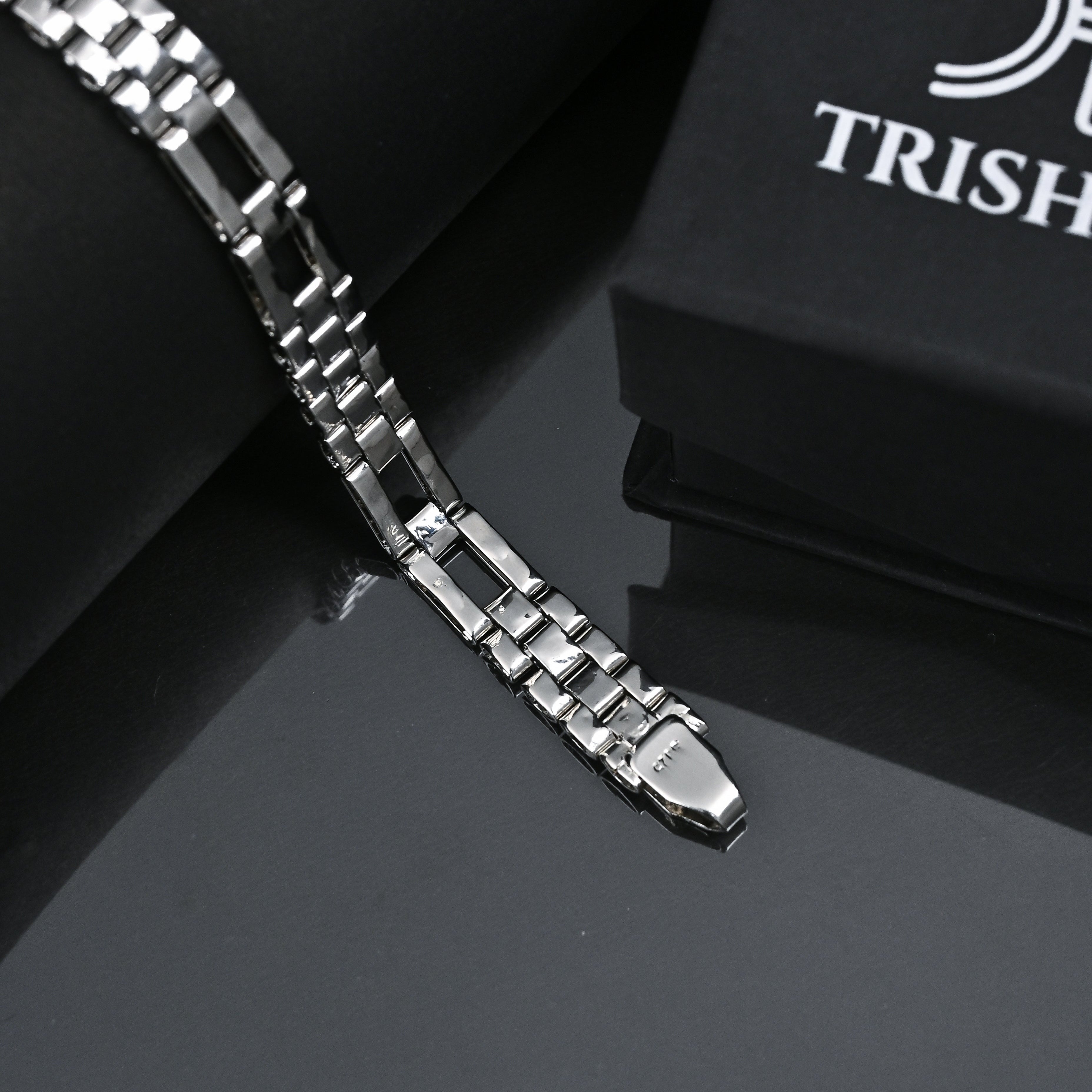 Silver bracelet on a reflective surface with 'Trishna' branding.