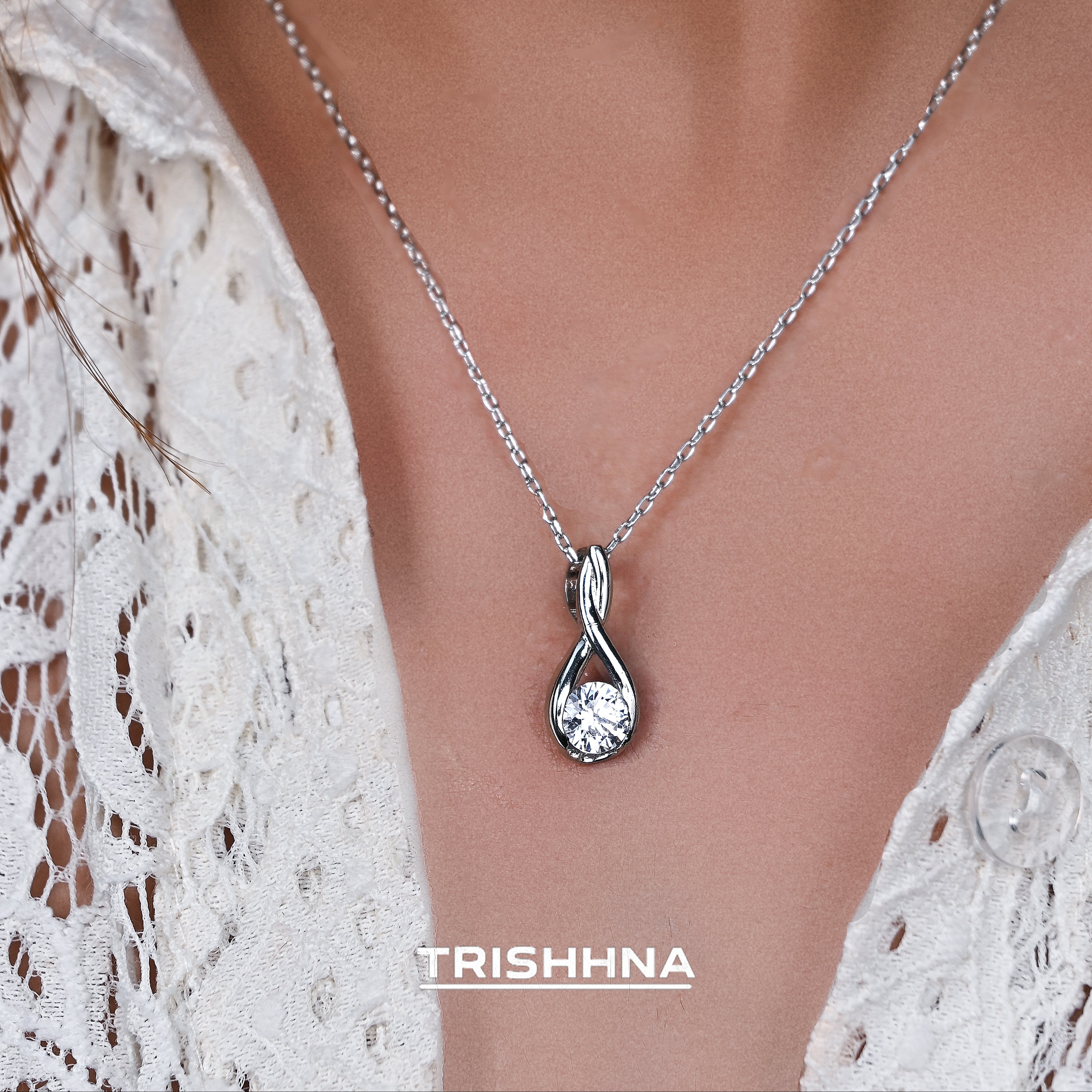 Silver necklace with a pendant on a person wearing a white lace garment, branded 'Trishnna'.