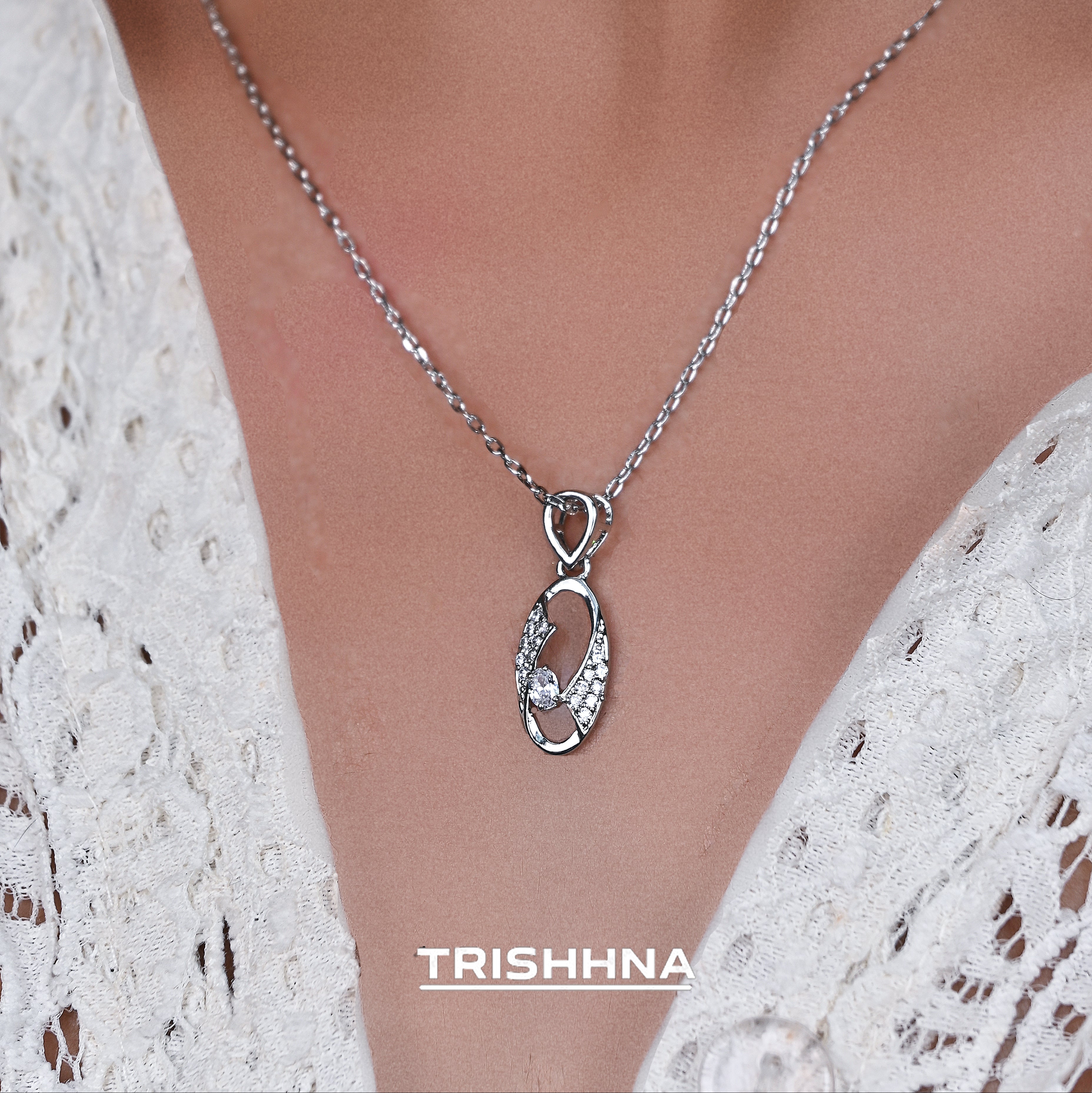Silver necklace with a pendant on a model wearing a white lace top, branded 'Trishna'.