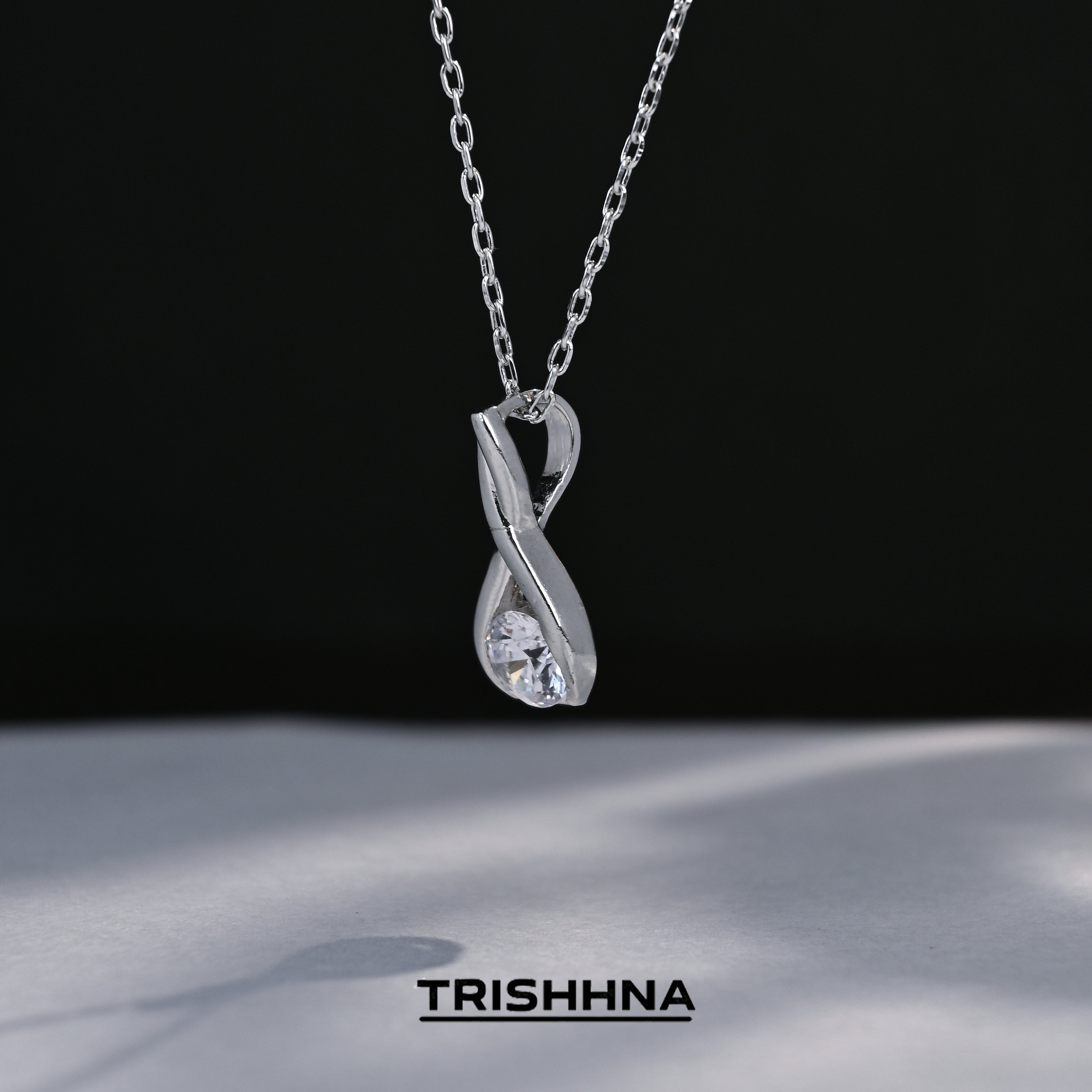 Silver necklace with a pendant on a black background, featuring the brand 'TRISHNHA'.