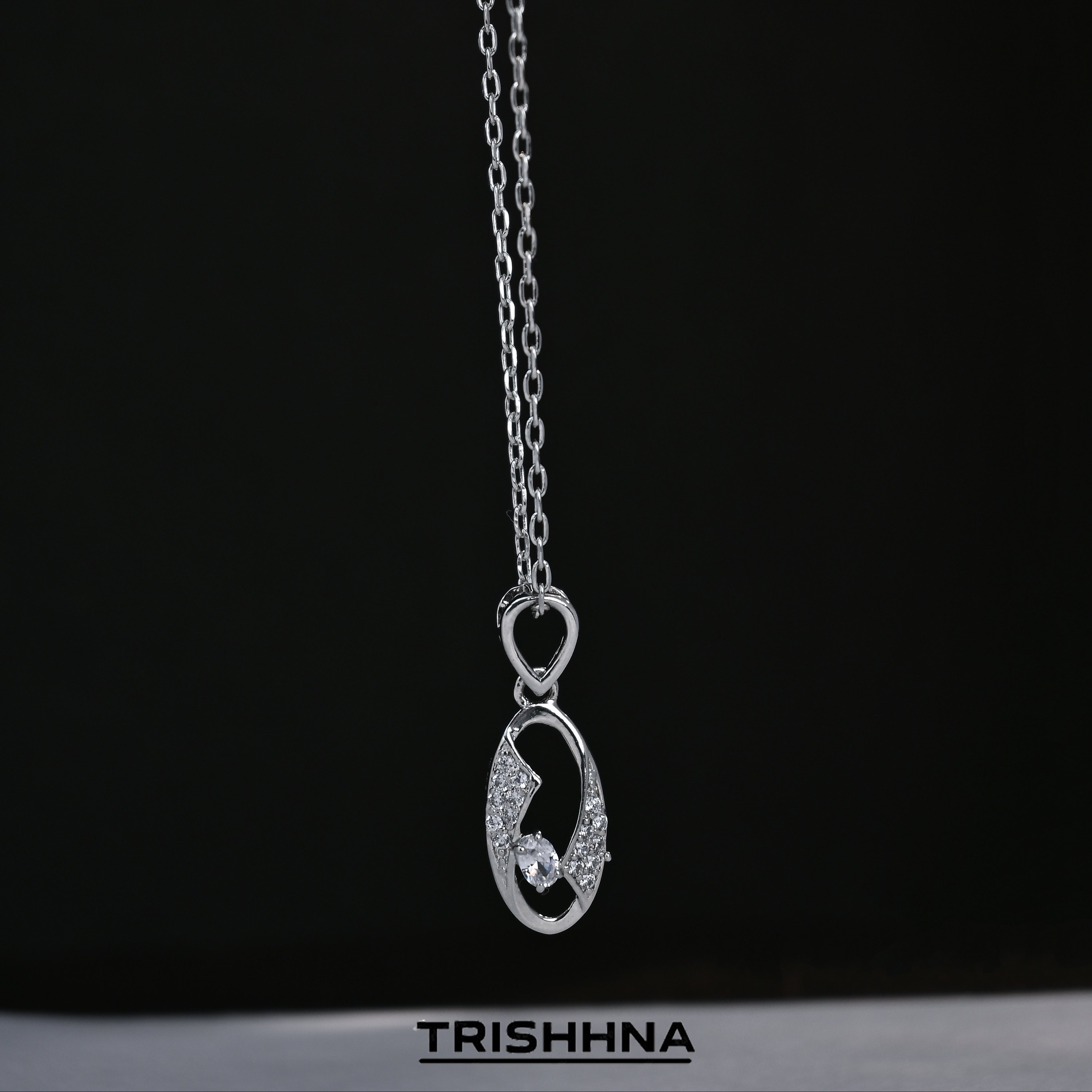 Silver necklace with a pendant on a black background, featuring the brand 'TRISHHNA'.