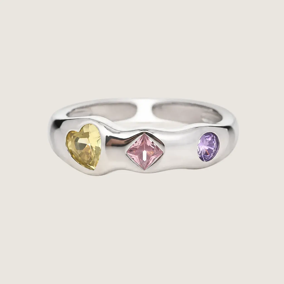 Silver ring with heart, square, and round gemstones on a beige background