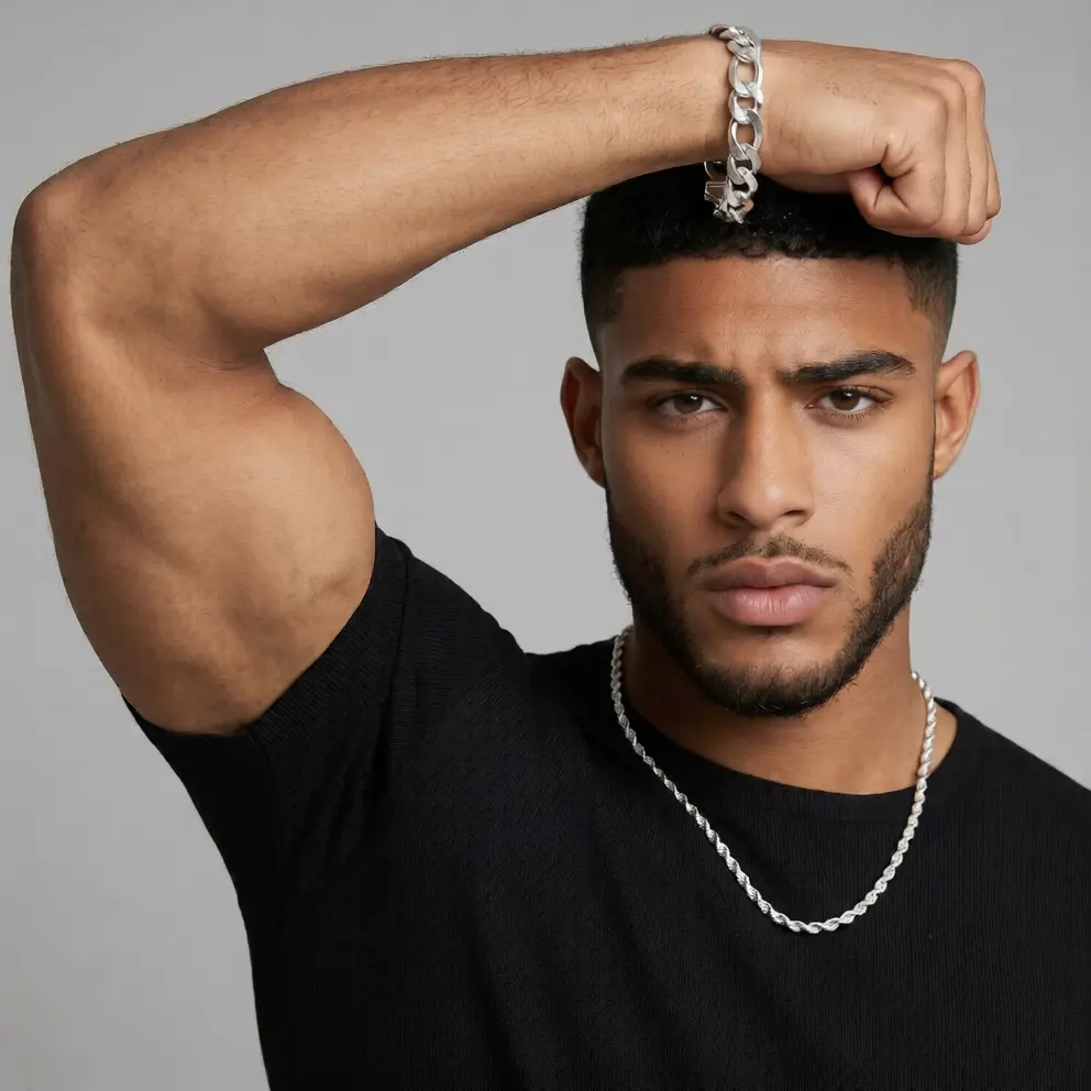Man wearing a black shirt and silver chain, posing with arm raised against a gray background