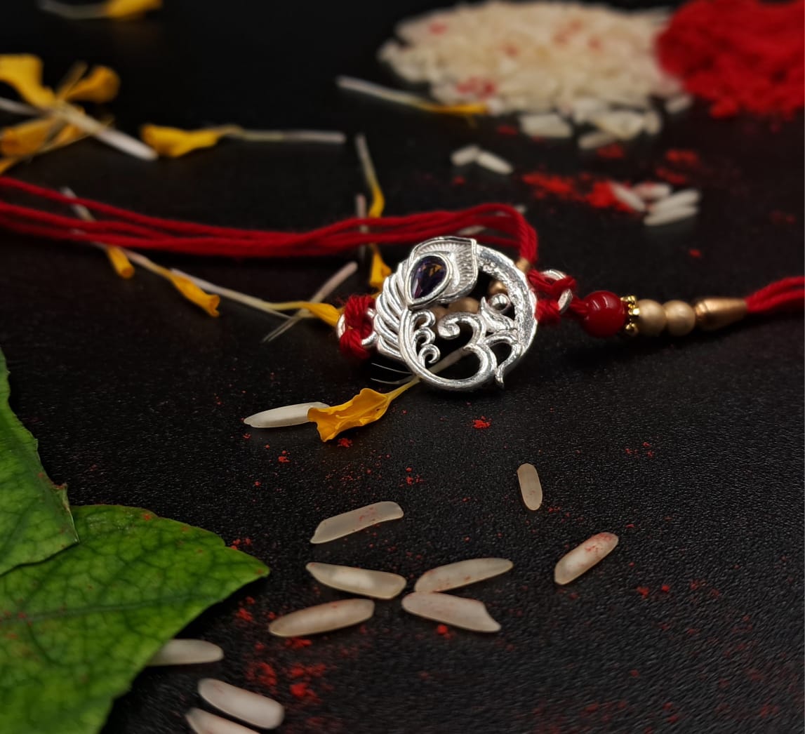 Silver Rakhi with red thread on a dark surface with leaves and seeds