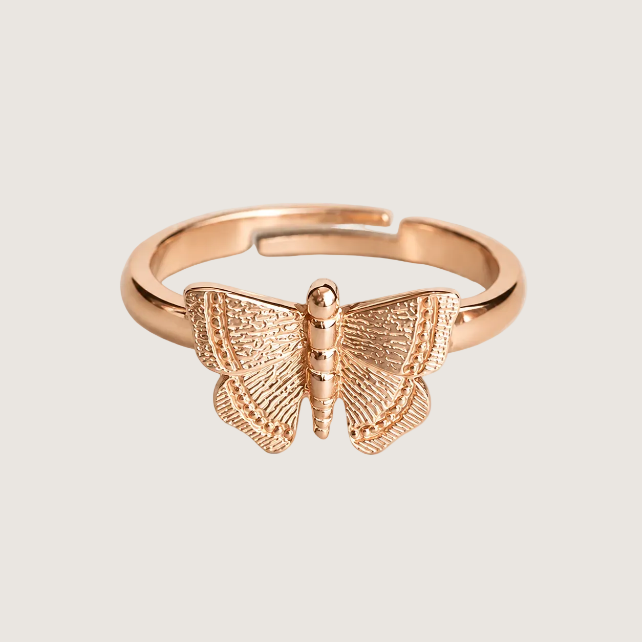 Rose gold butterfly ring on a light beige background