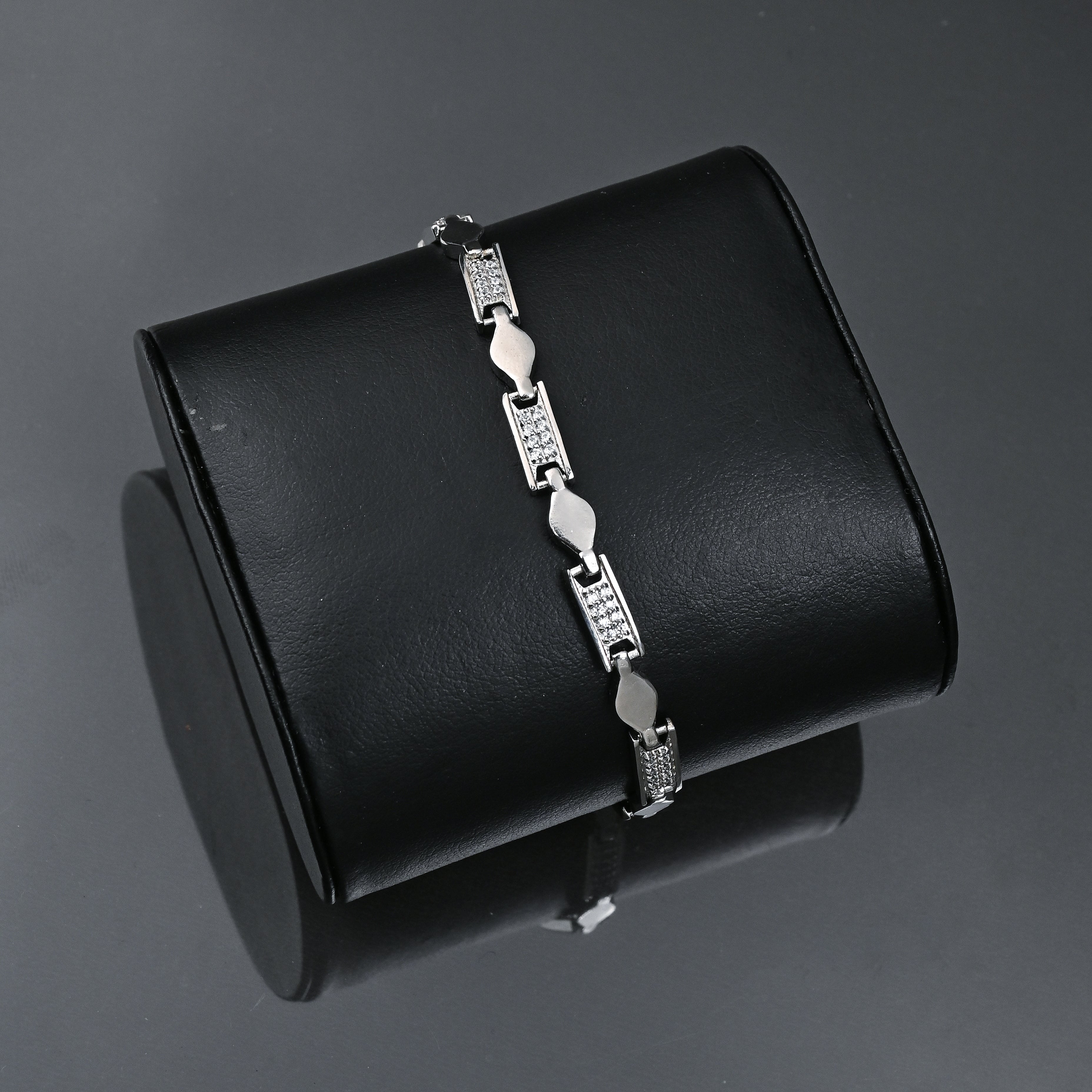 Silver bracelet on a black stand with 'TRISHNHA' branding.