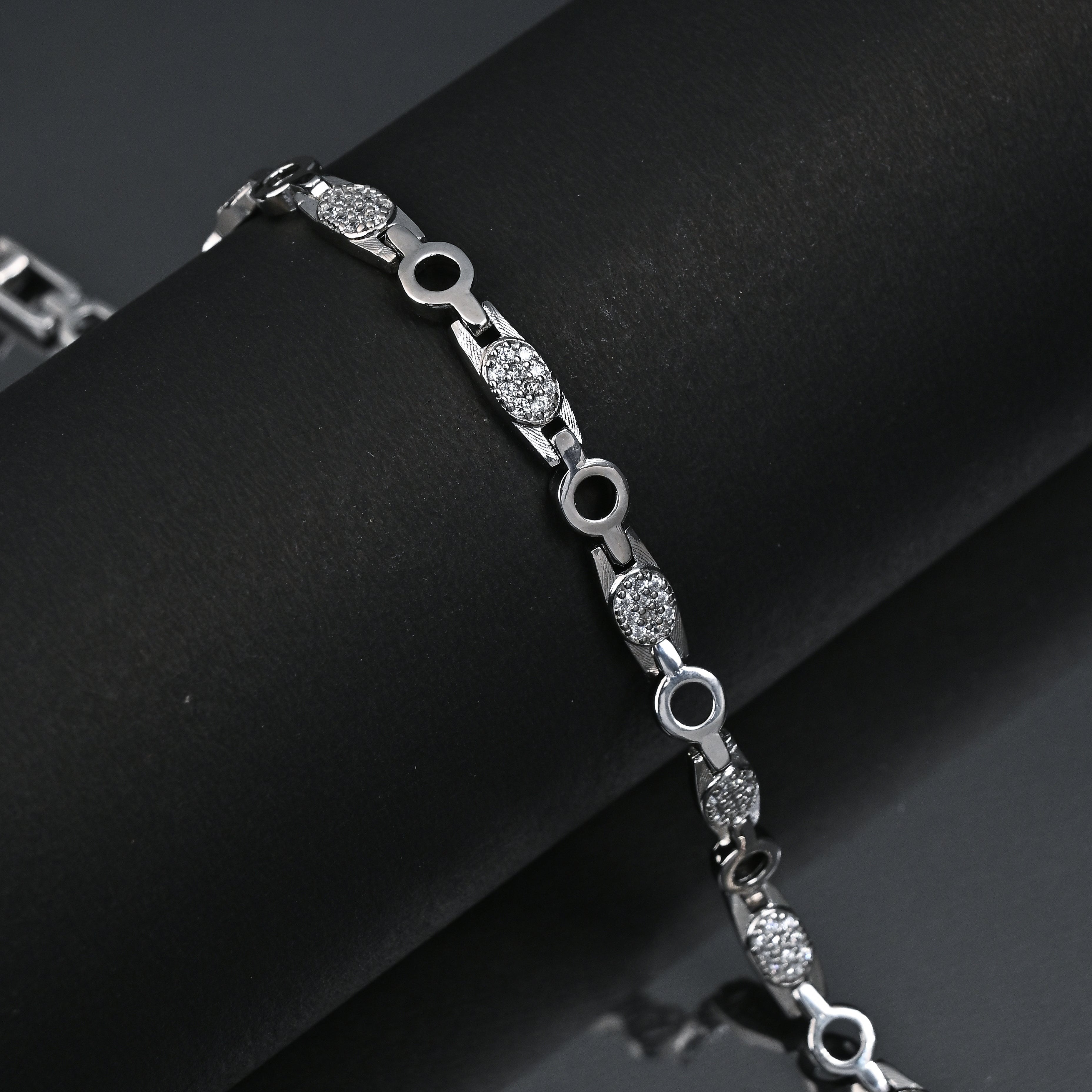 Silver bracelet with embedded stones on a black surface, featuring the Trishna brand.