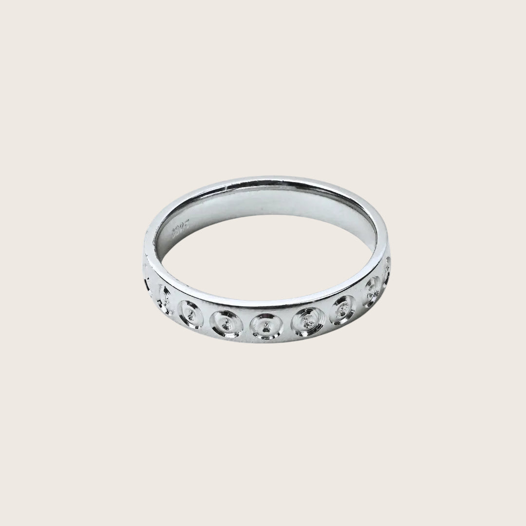 Silver ring with small stones on a white background, branded 'TRISHNNA'.