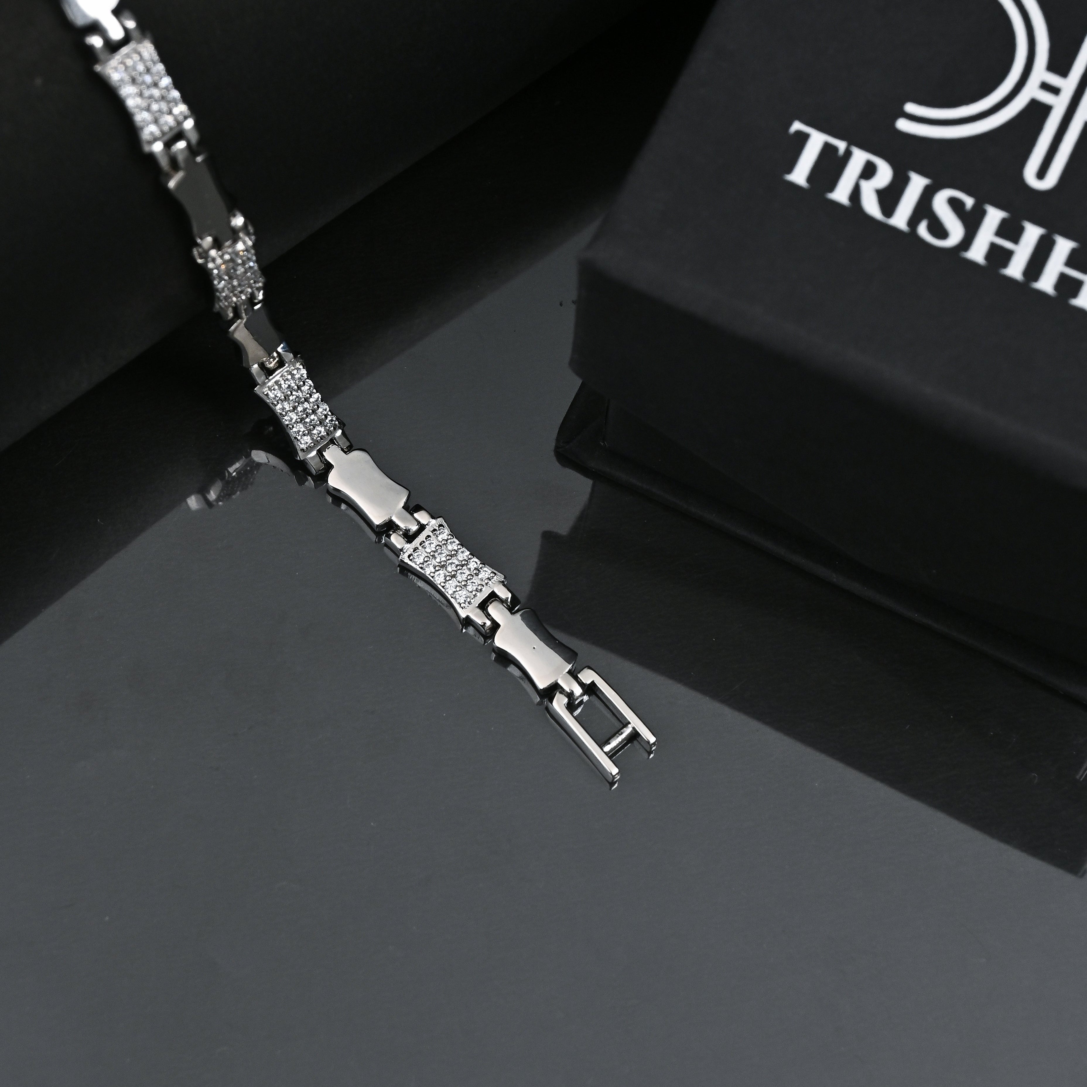 Silver bracelet with diamond accents on a reflective surface, branded 'Trishhna'.