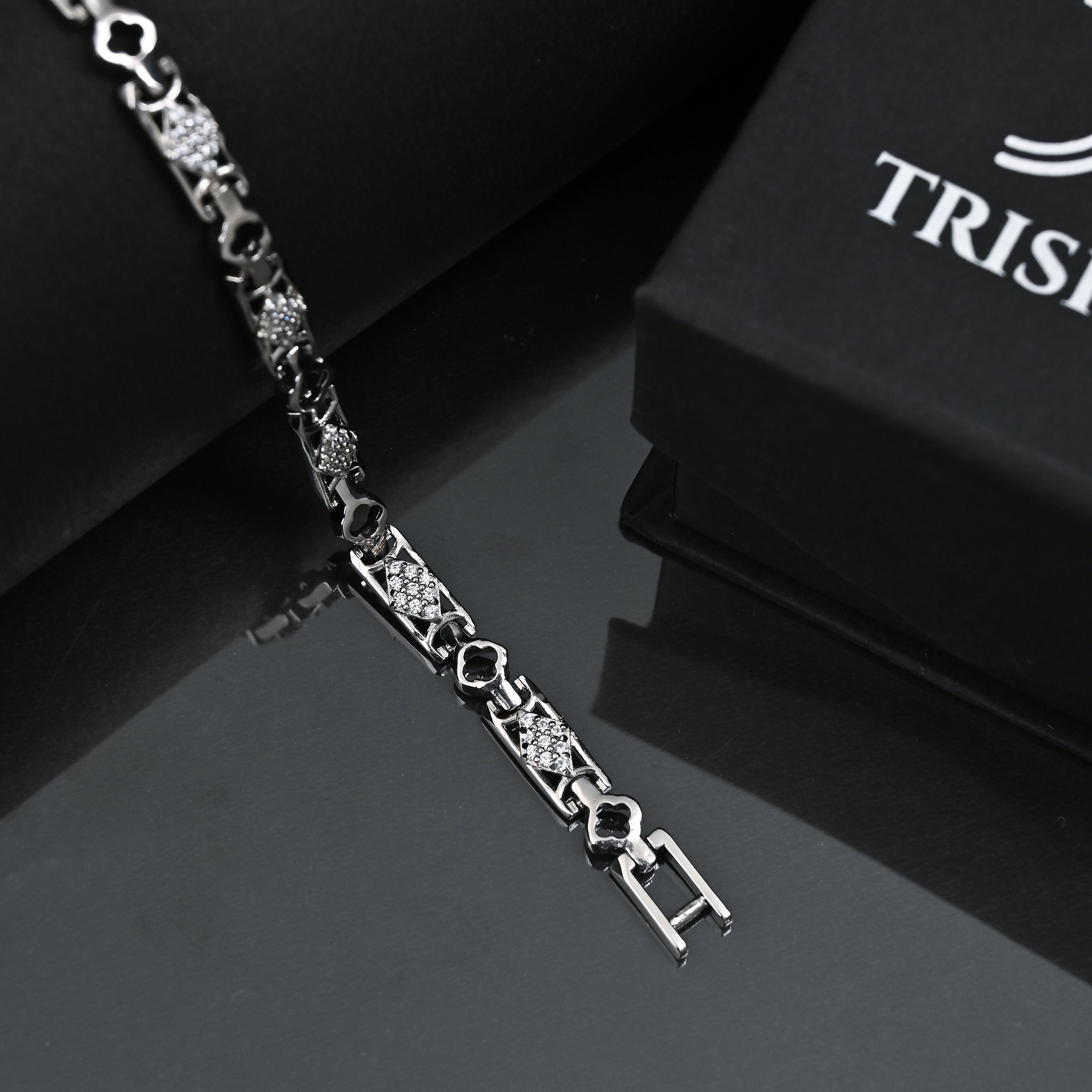 Silver bracelet with intricate design on a reflective surface, Trishhna branding visible.