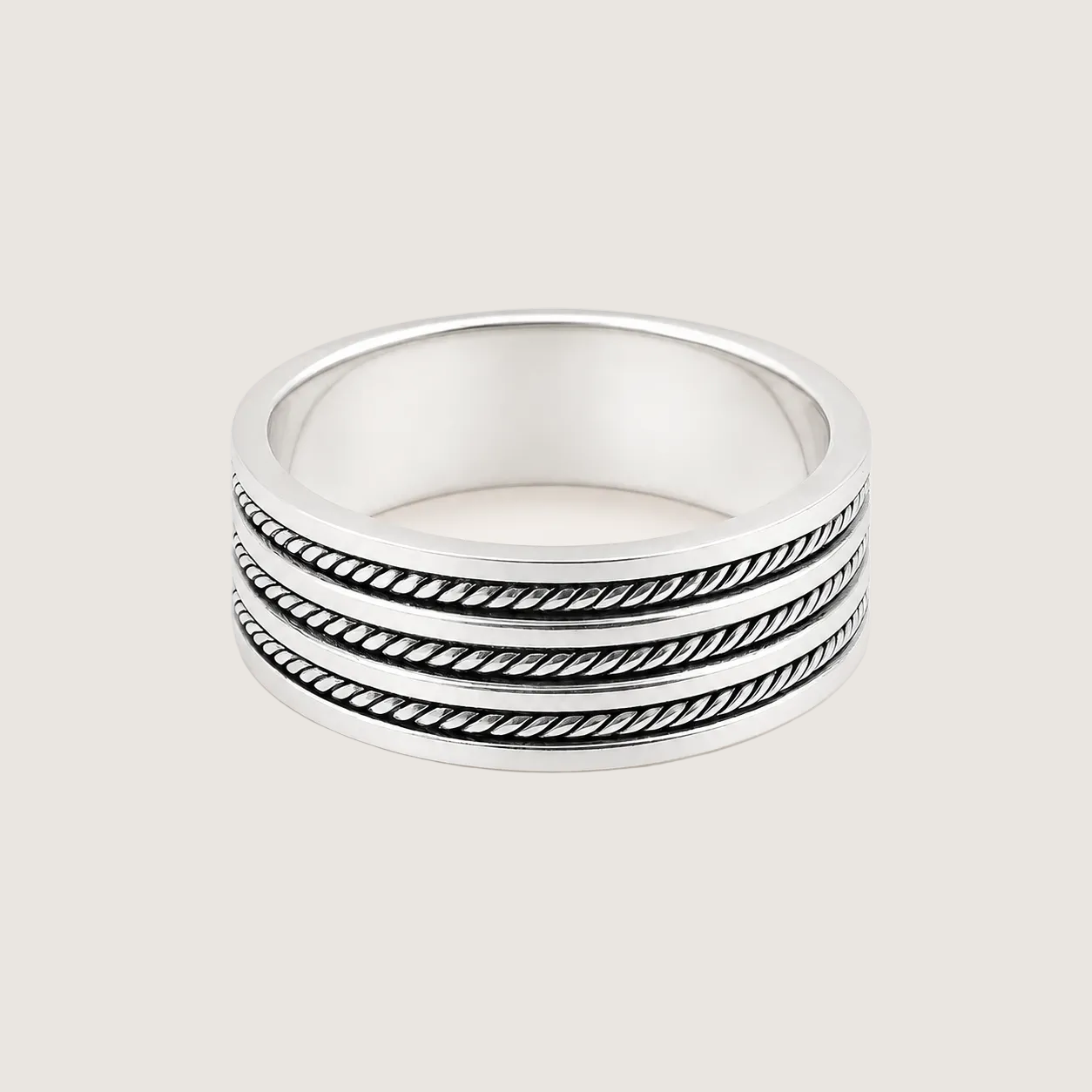 Stack of three silver rings with textured band design on a light beige background