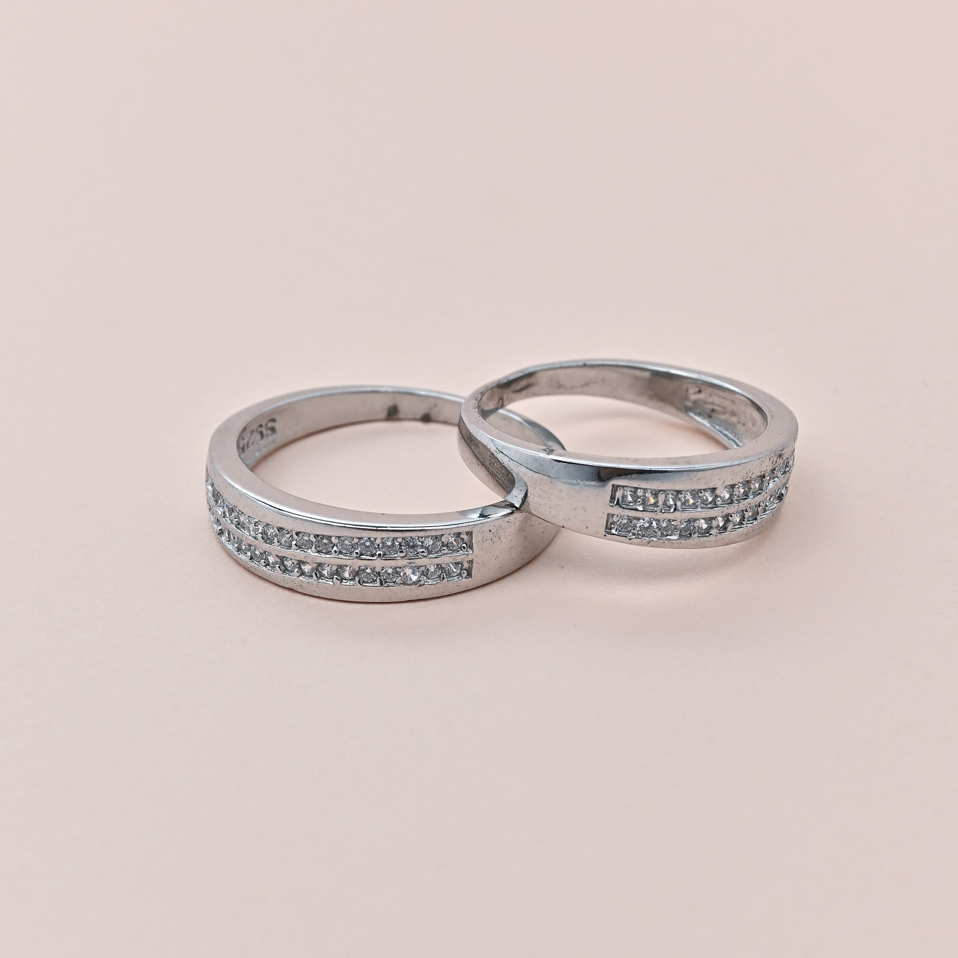 Two silver rings with small stones on a beige background, featuring the brand 'Trishhna'.