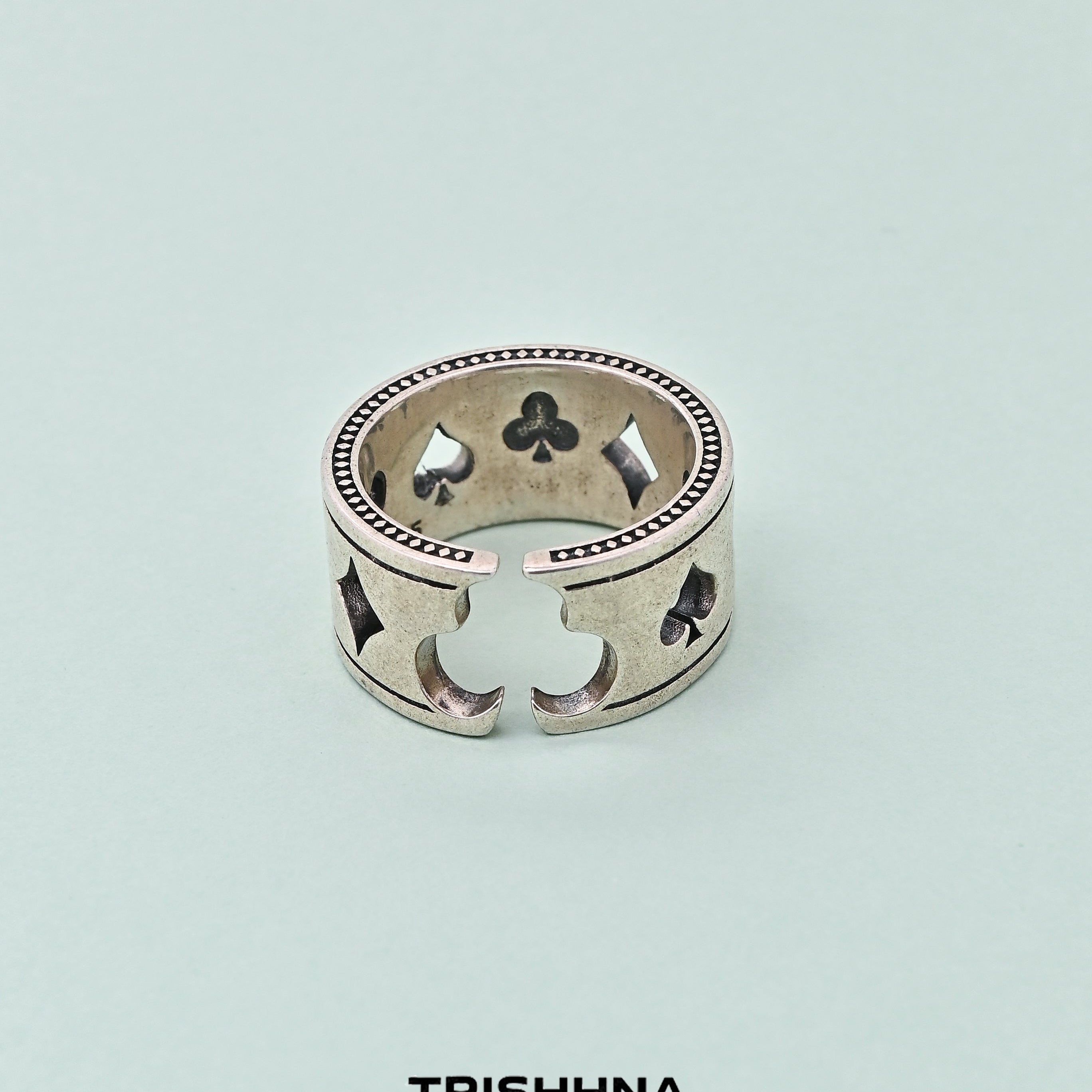 Silver ring with clover designs on a light blue background, branded 'TRISHHNA'.
