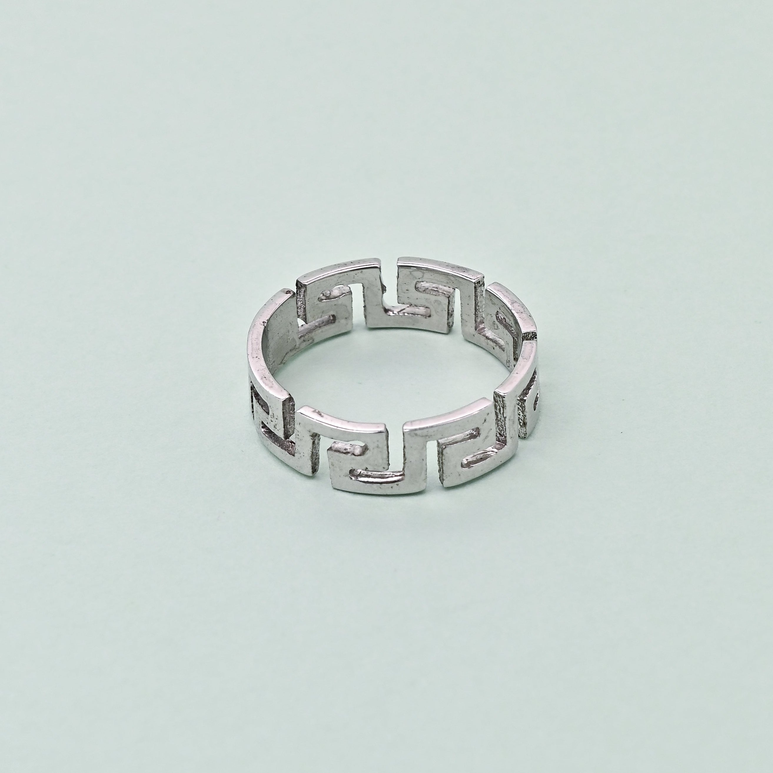 Silver ring with geometric design on a light blue background, featuring the brand 'TRISHNHA'.