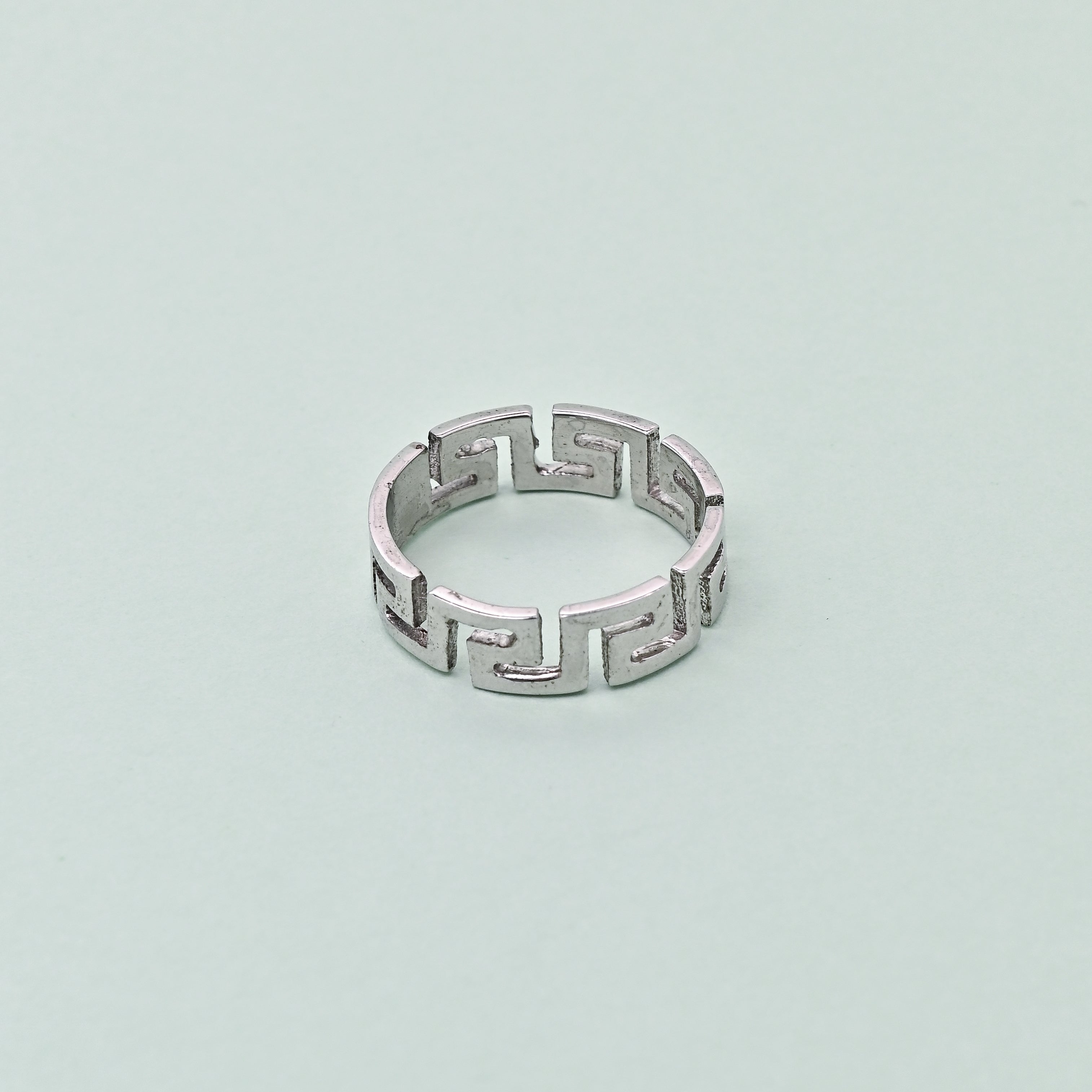 Silver ring with geometric design on a light blue background, featuring the brand 'TRISHNHA'.