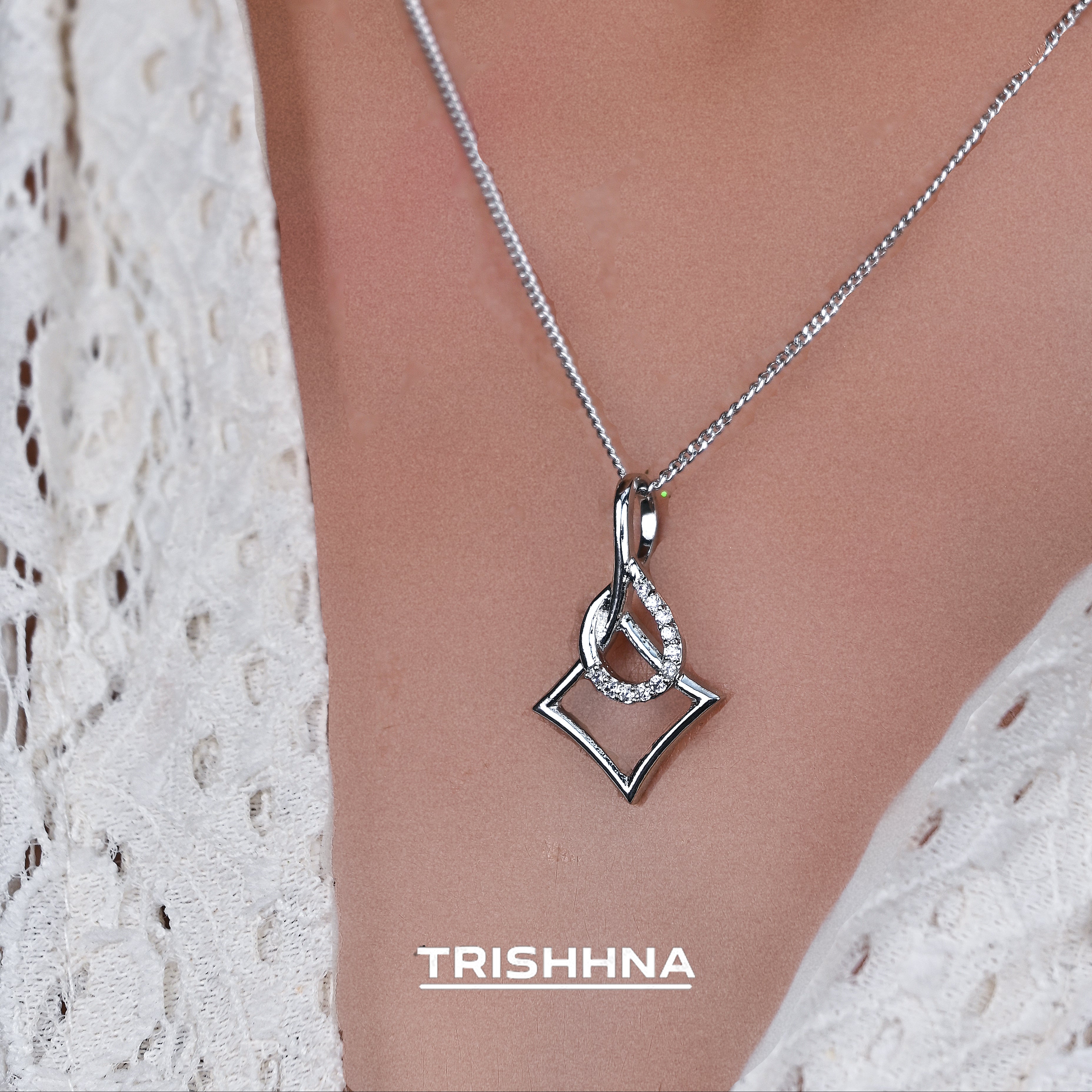 Silver necklace with a pendant on a person wearing a white lace top, branded 'Trishnna'.