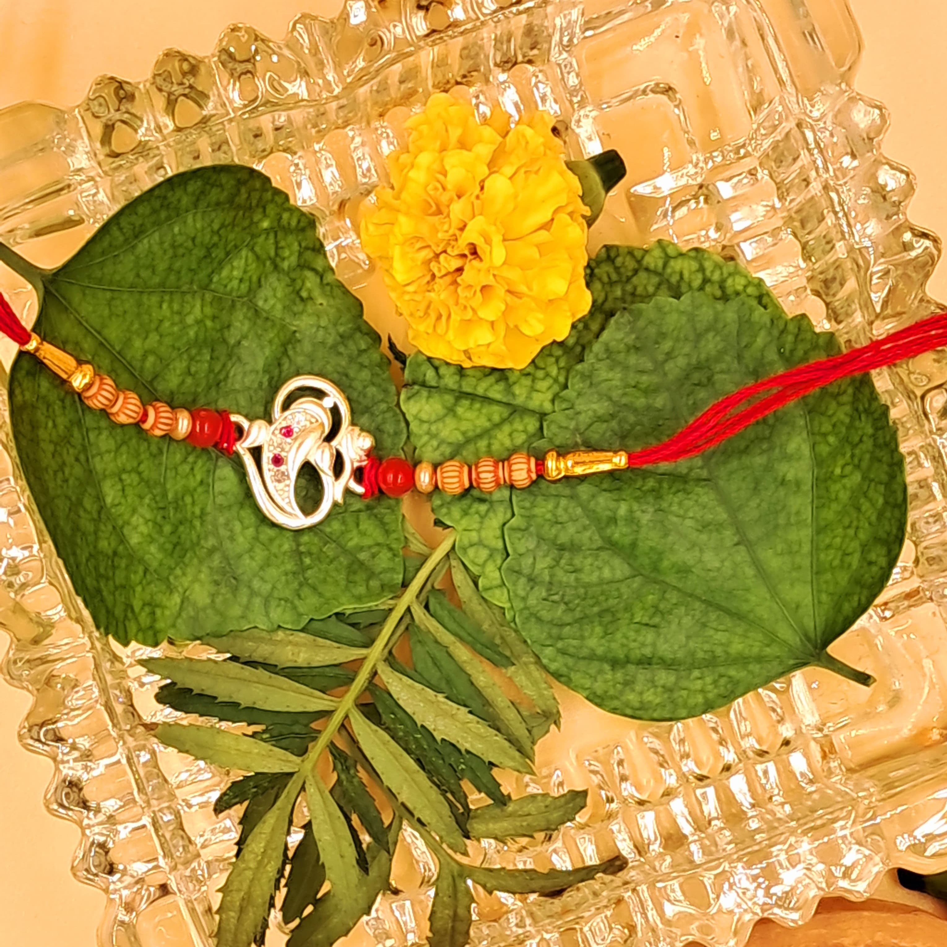 Rakhi with yellow flower and green leaves on a decorative glass plate.