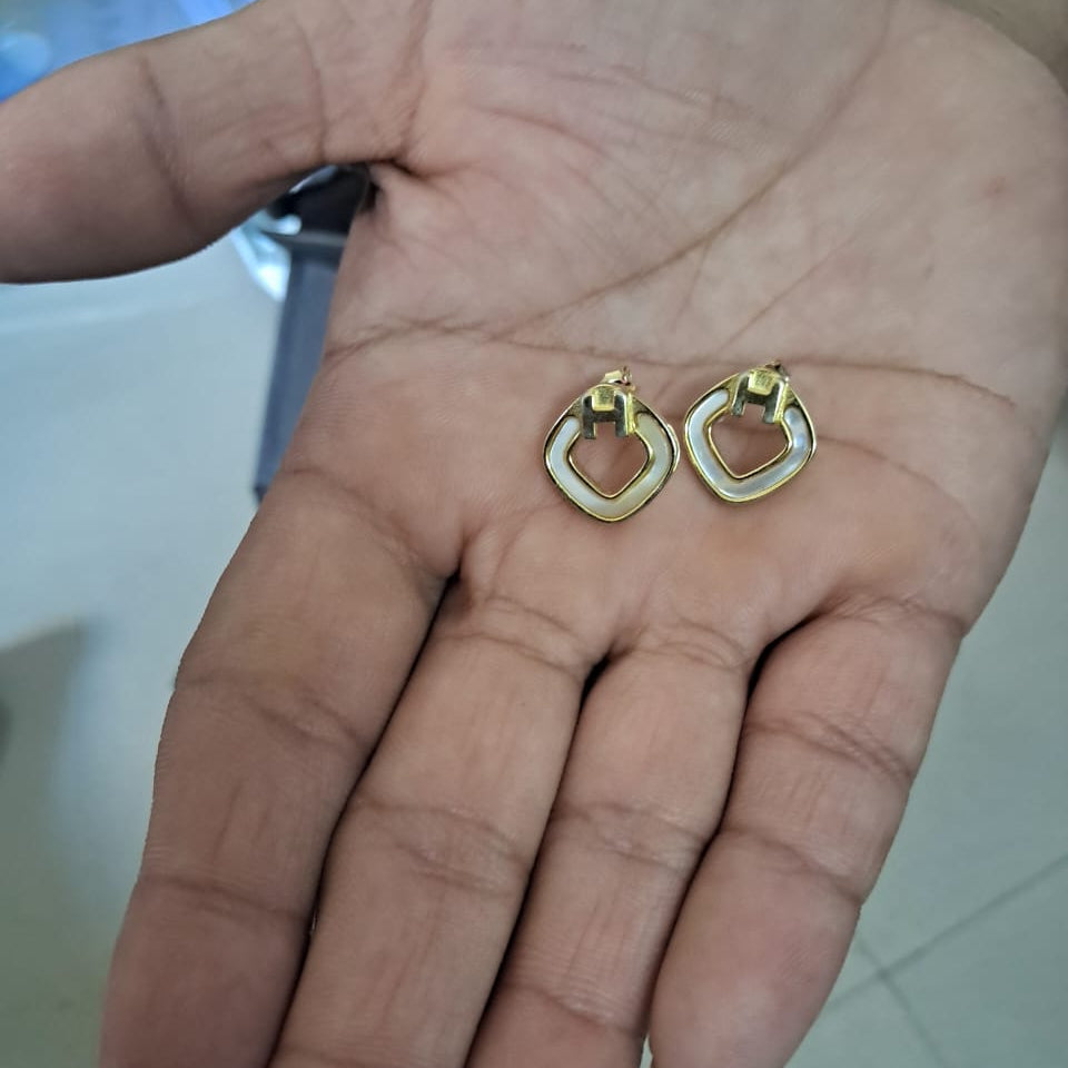 Gold hoop earrings held in a hand with a blurred background