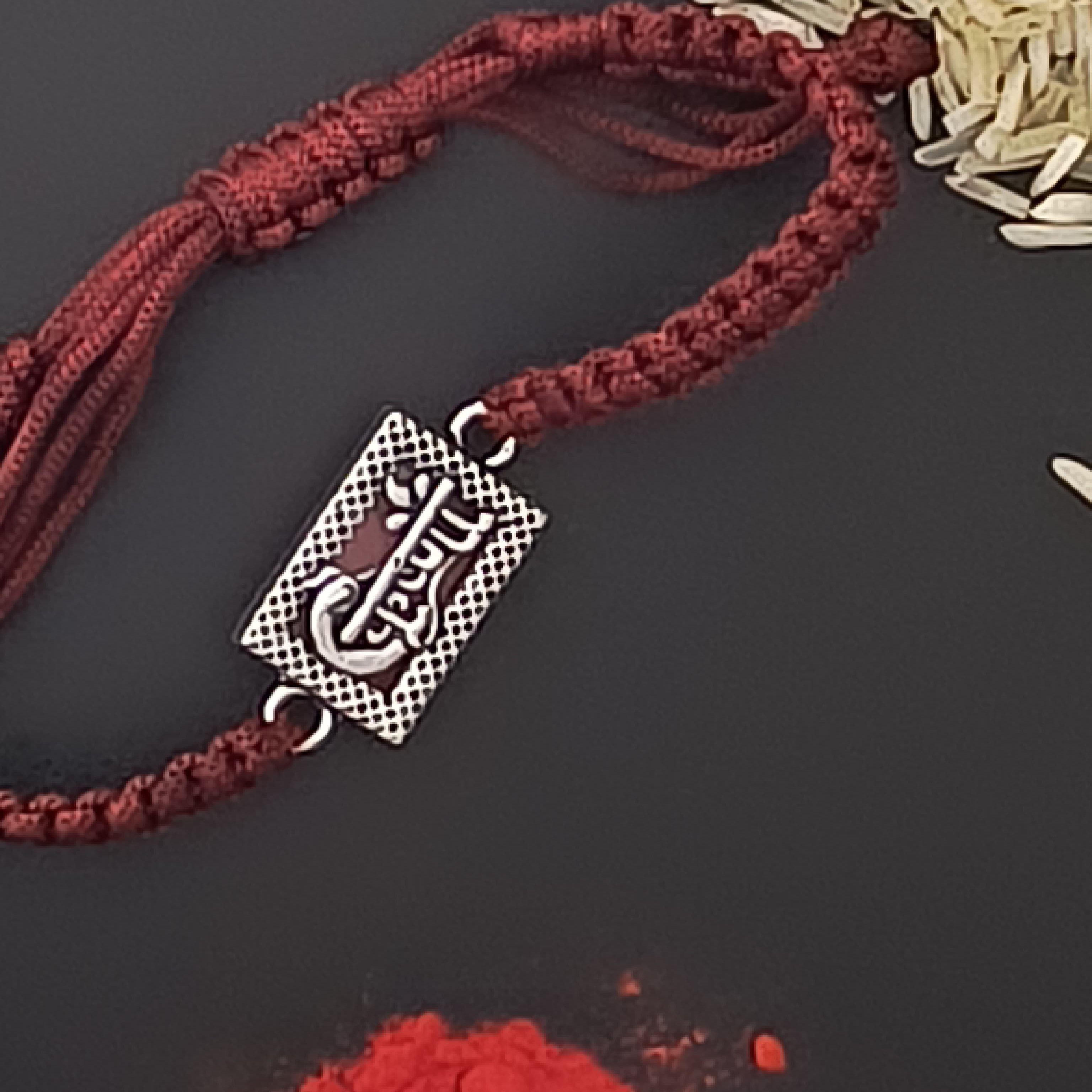 Bracelet with a silver charm on a dark surface with rice and red powder