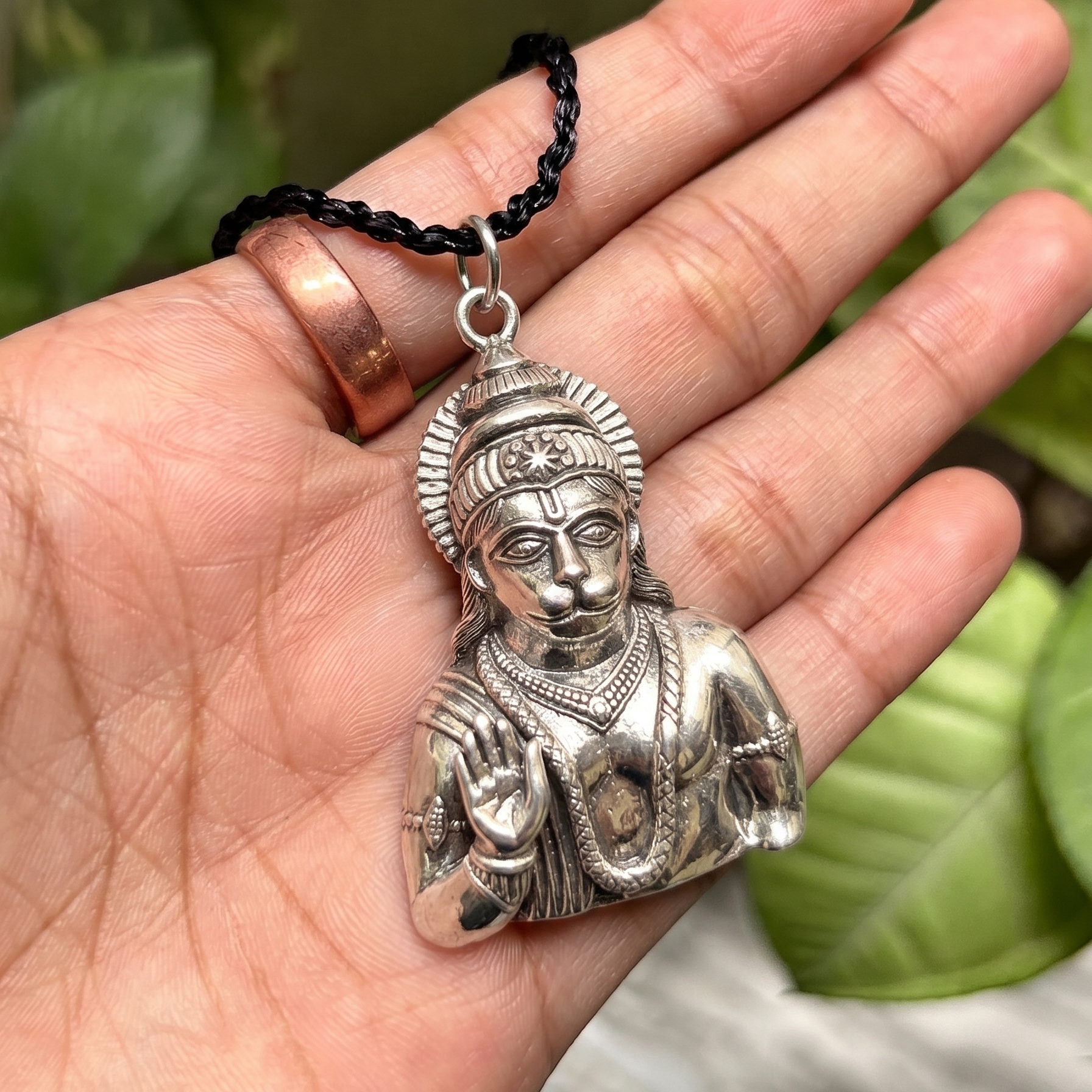 Silver pendant of a seated figure held in a hand with a blurred green leafy background