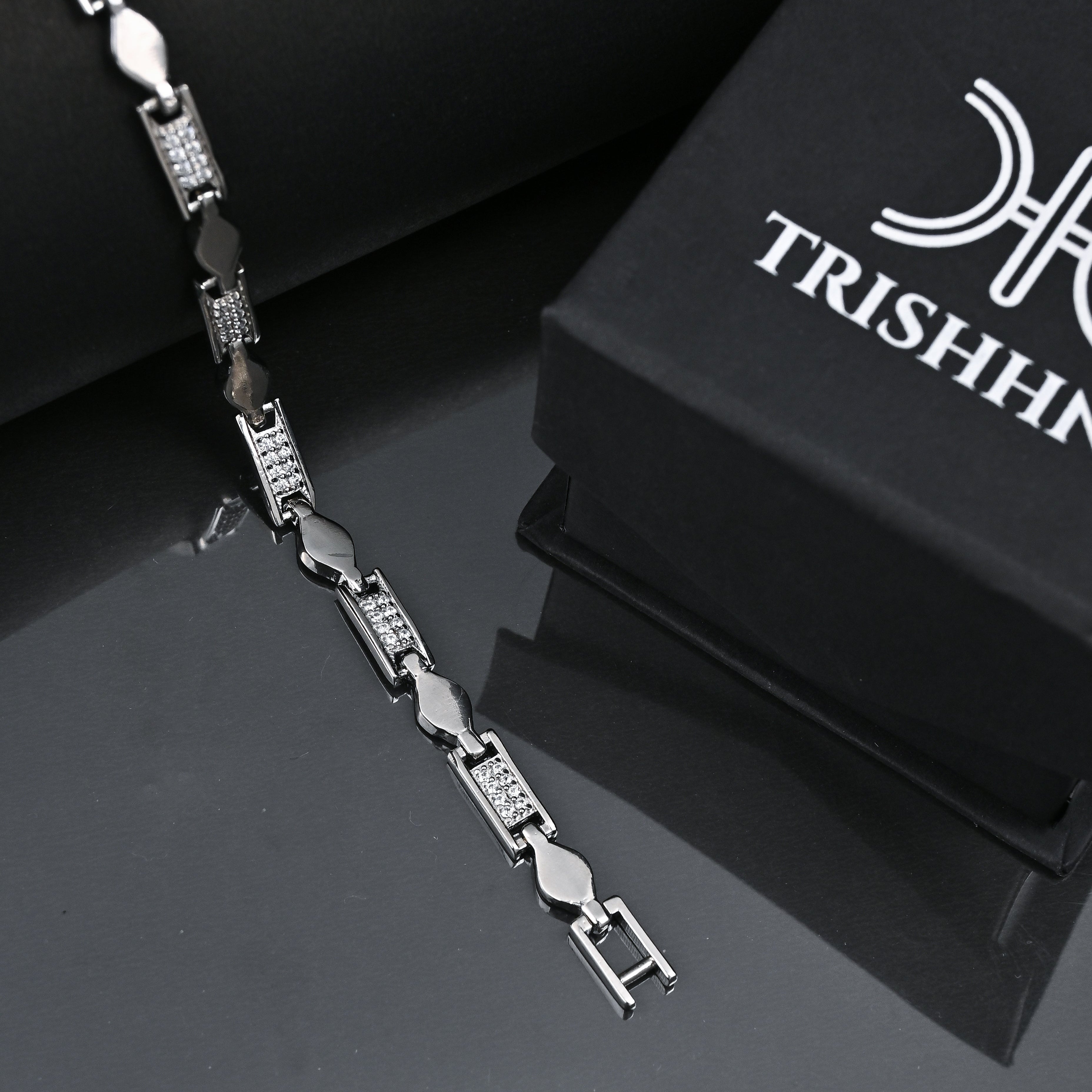 Silver bracelet with black beads on a reflective surface next to a black box with 'TRISHHNA' branding.