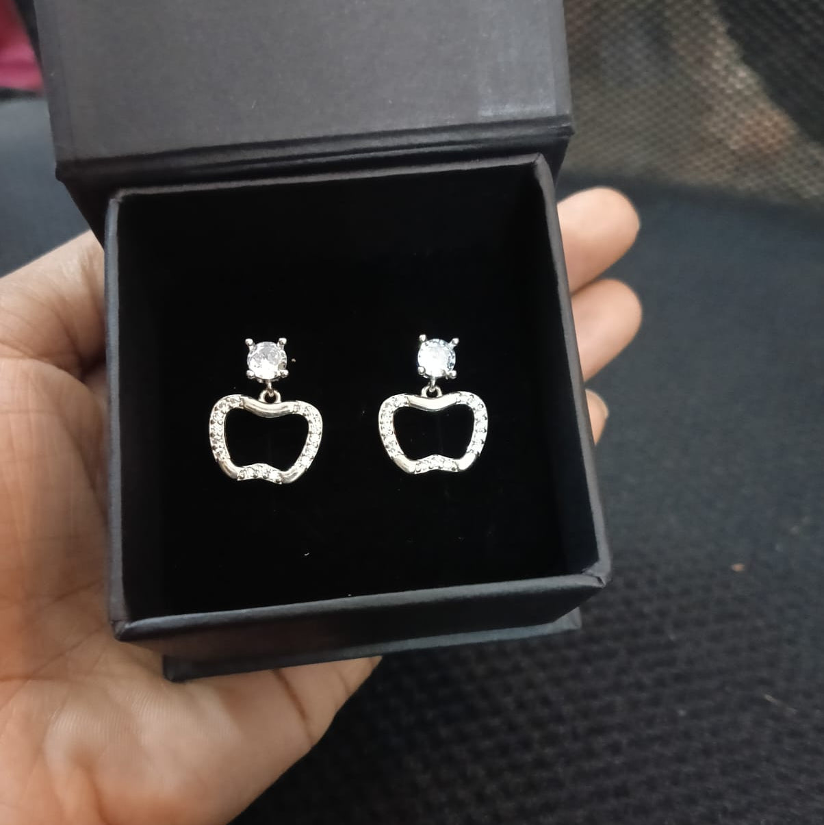 Silver earrings in a black jewelry box held in a hand.