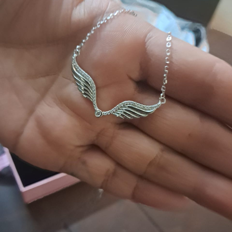 Silver wing-shaped necklace on a hand with a blurred background