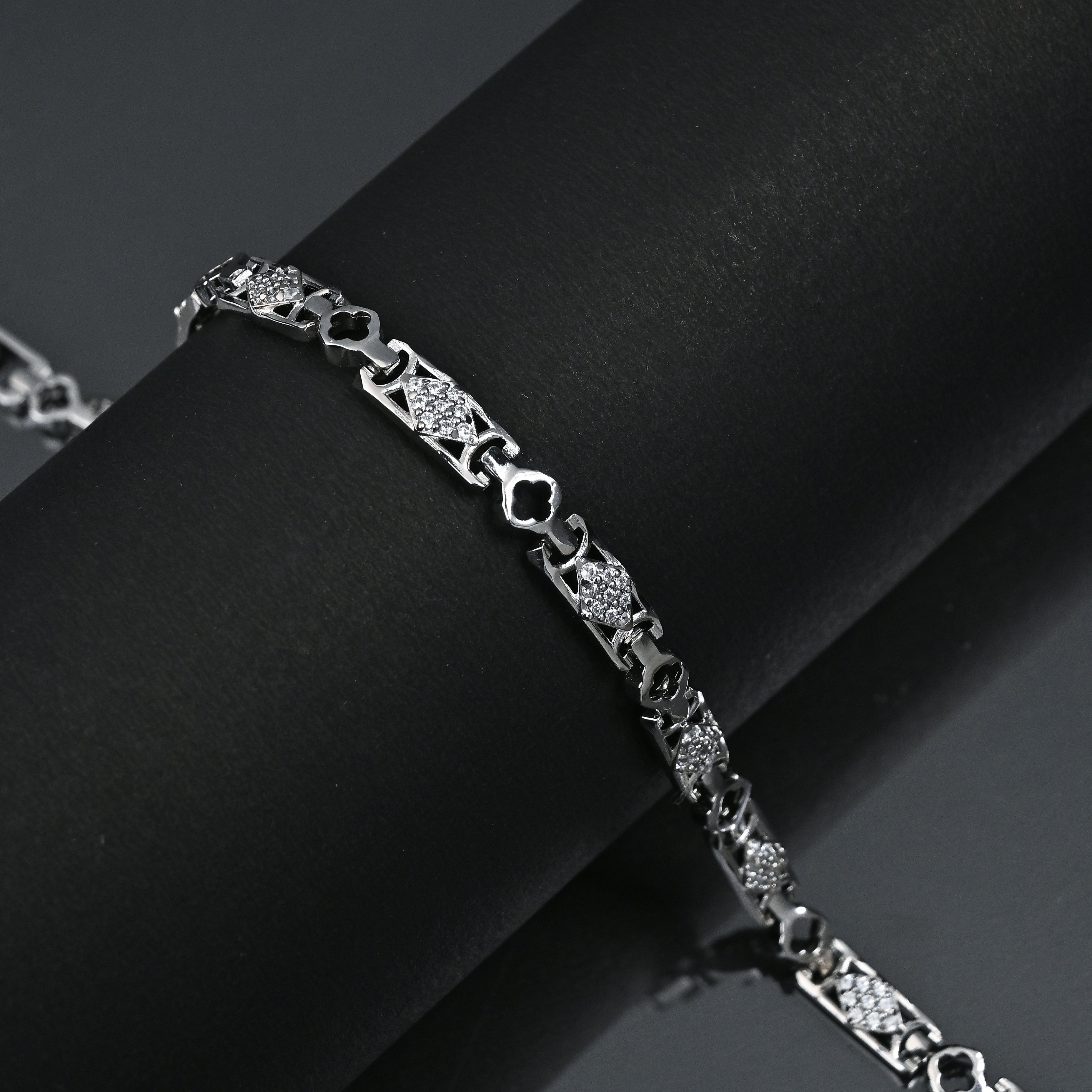 Silver bracelet with intricate design on a black fabric background, featuring the brand 'Trishhna'.