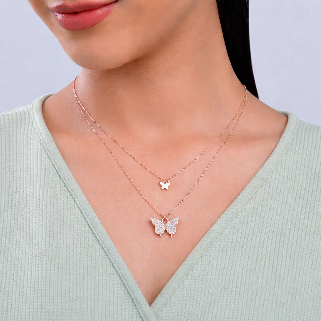 Close-up of a person wearing two butterfly-shaped necklaces on a light background