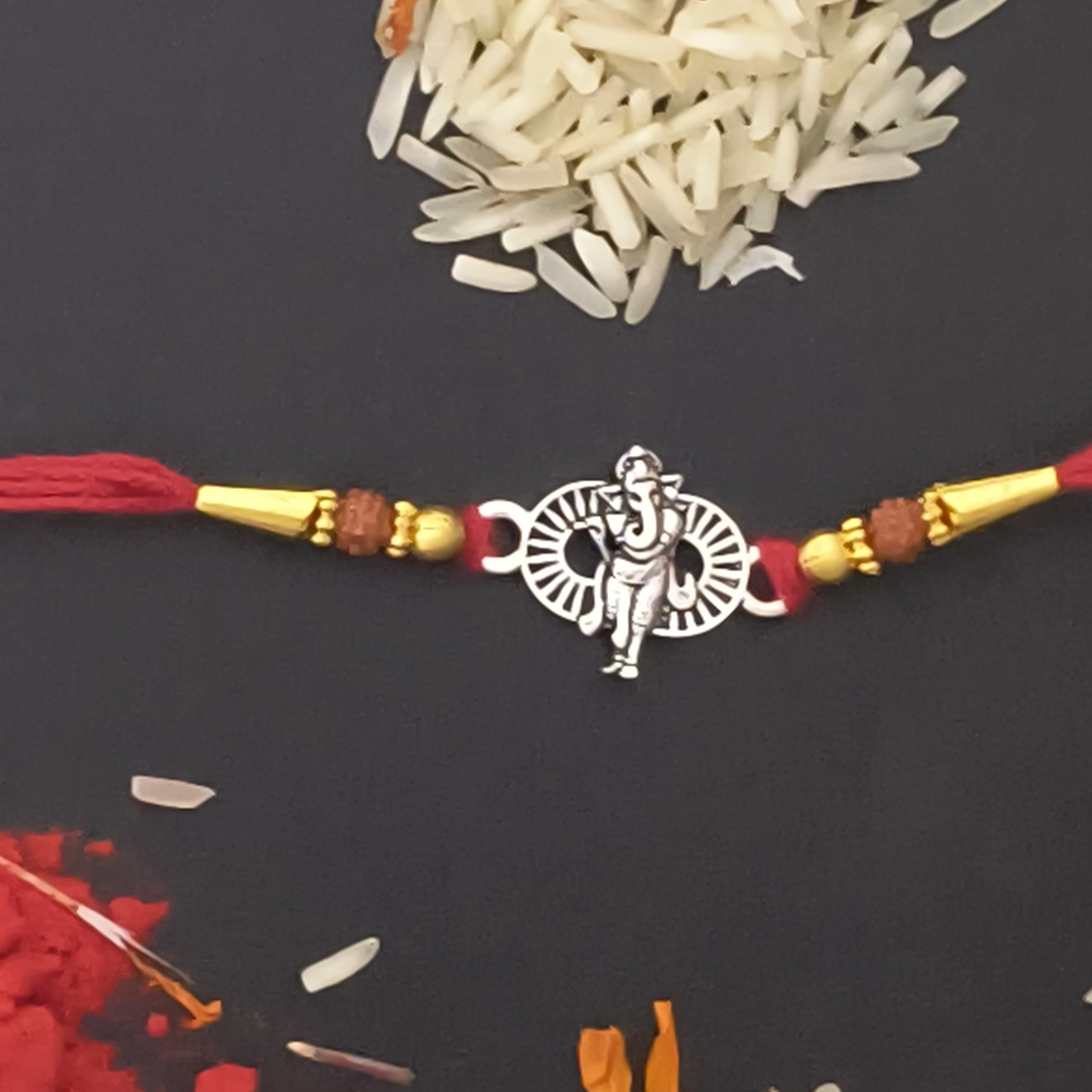 Decorative bracelet with a silver pendant on a dark surface with rice and red powder.